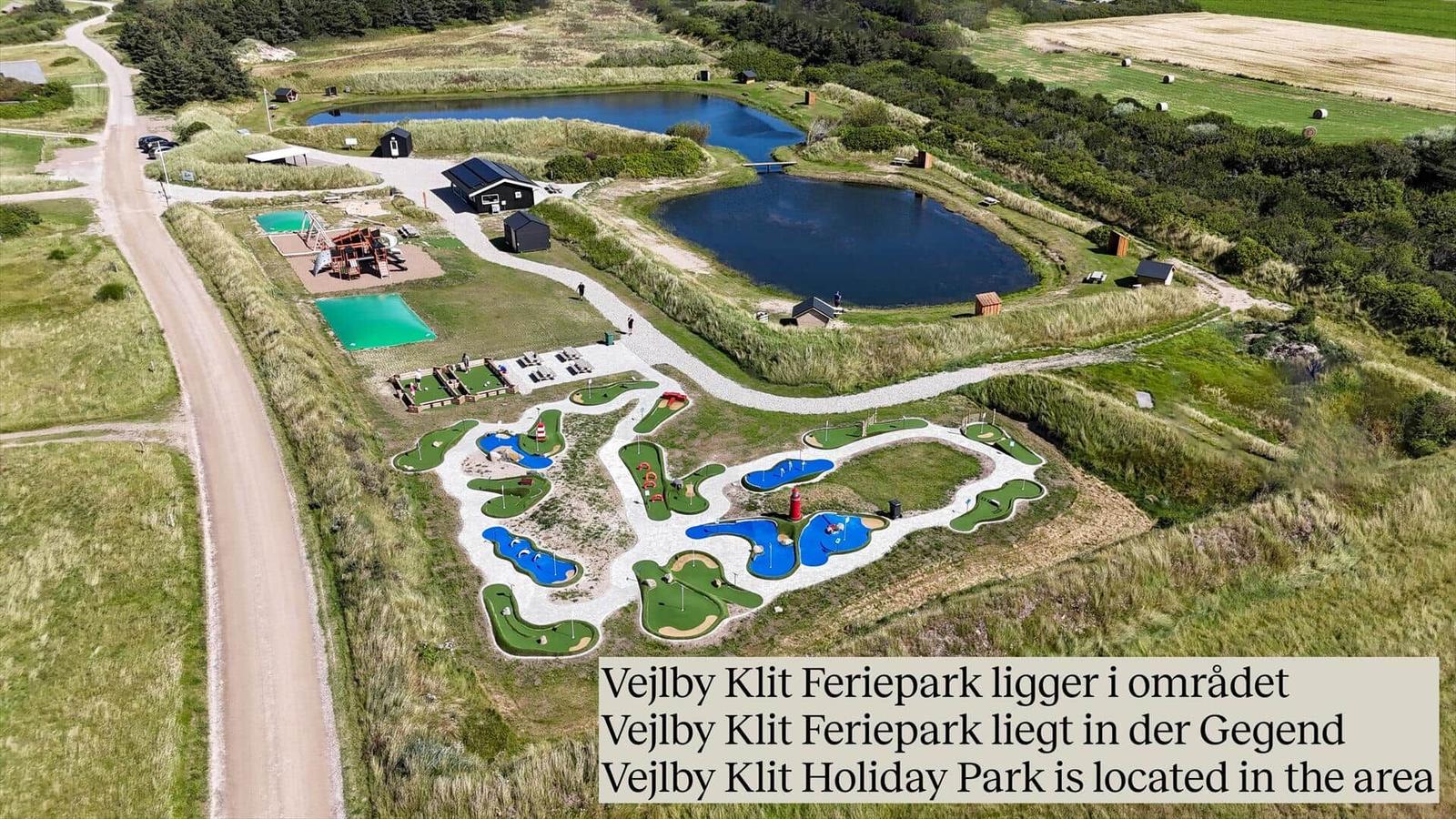 Aerial view of Vejlby Klit Holiday Park with mini golf, ponds, and cabins.