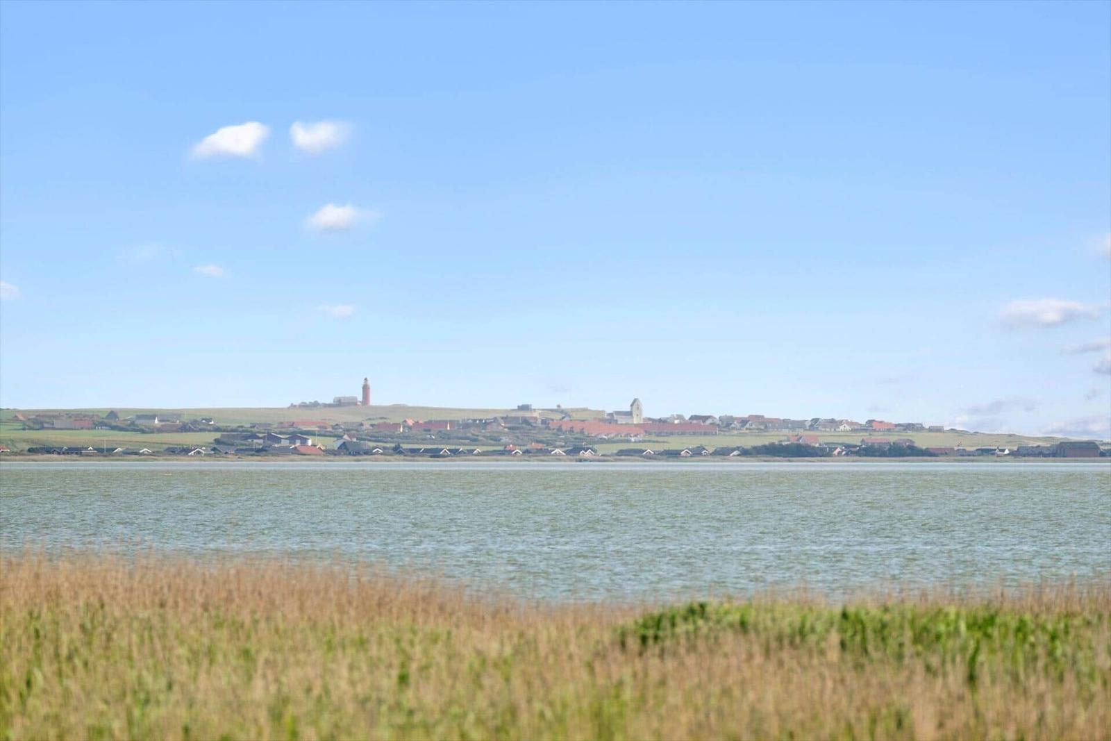 Weitläufiger Blick auf Wasser und Küstenstadt mit Leuchtturm im Hintergrund.