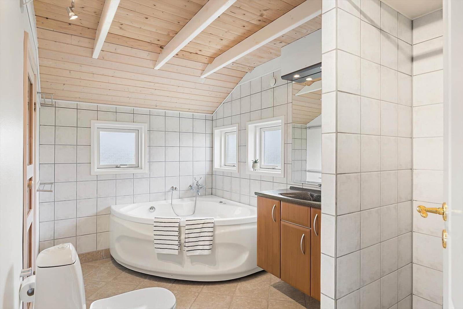Badezimmer mit Badewanne, Waschbecken und Toilette. Holzdecke und Fliesenwände.