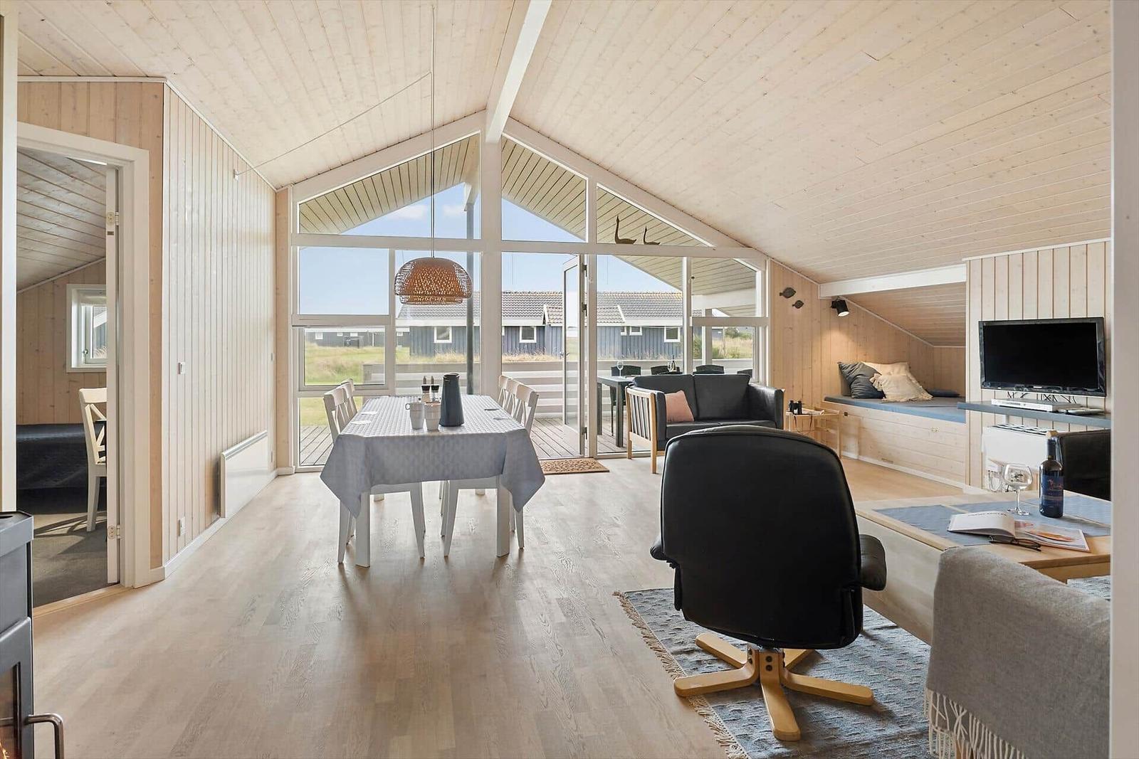 Wohn- und Essbereich mit großem Fenster, Sofa, TV und Esstisch.