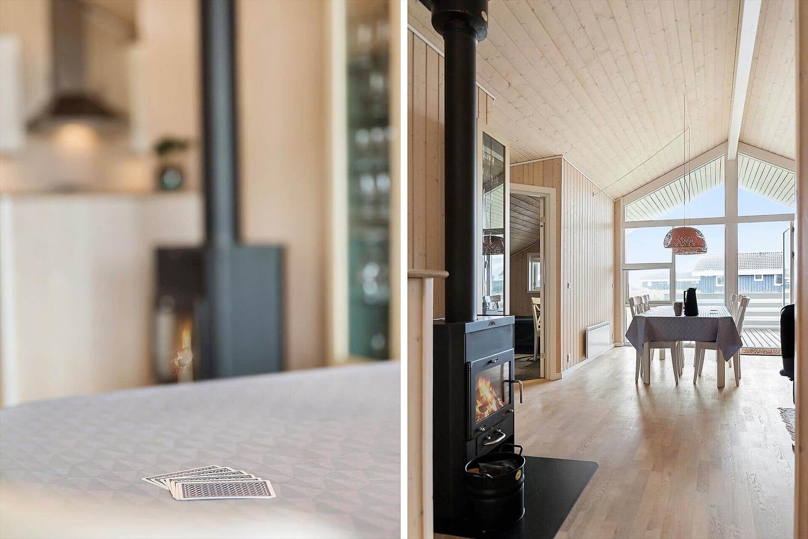 Küche mit Holzvertäfelung und Esstisch mit Tischdecke. Kaminofen mit brennendem Feuer.