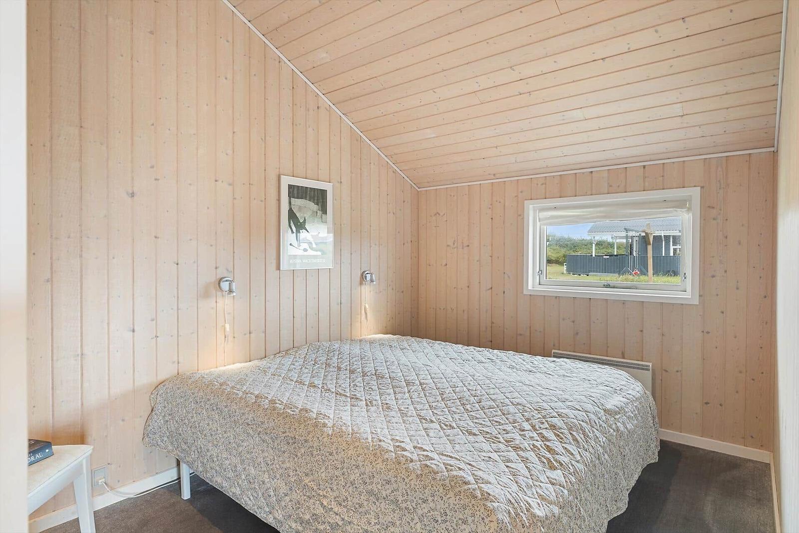 Schlafzimmer mit Holzwand, Bett und Fenster. Wandlampe und Bild an der Wand.