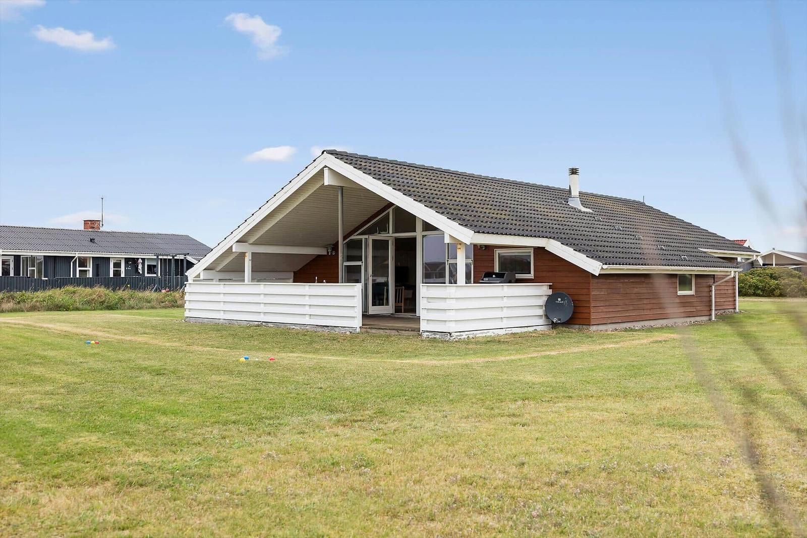Ein Haus mit braunem Holz und weißer Veranda auf grünem Grund.