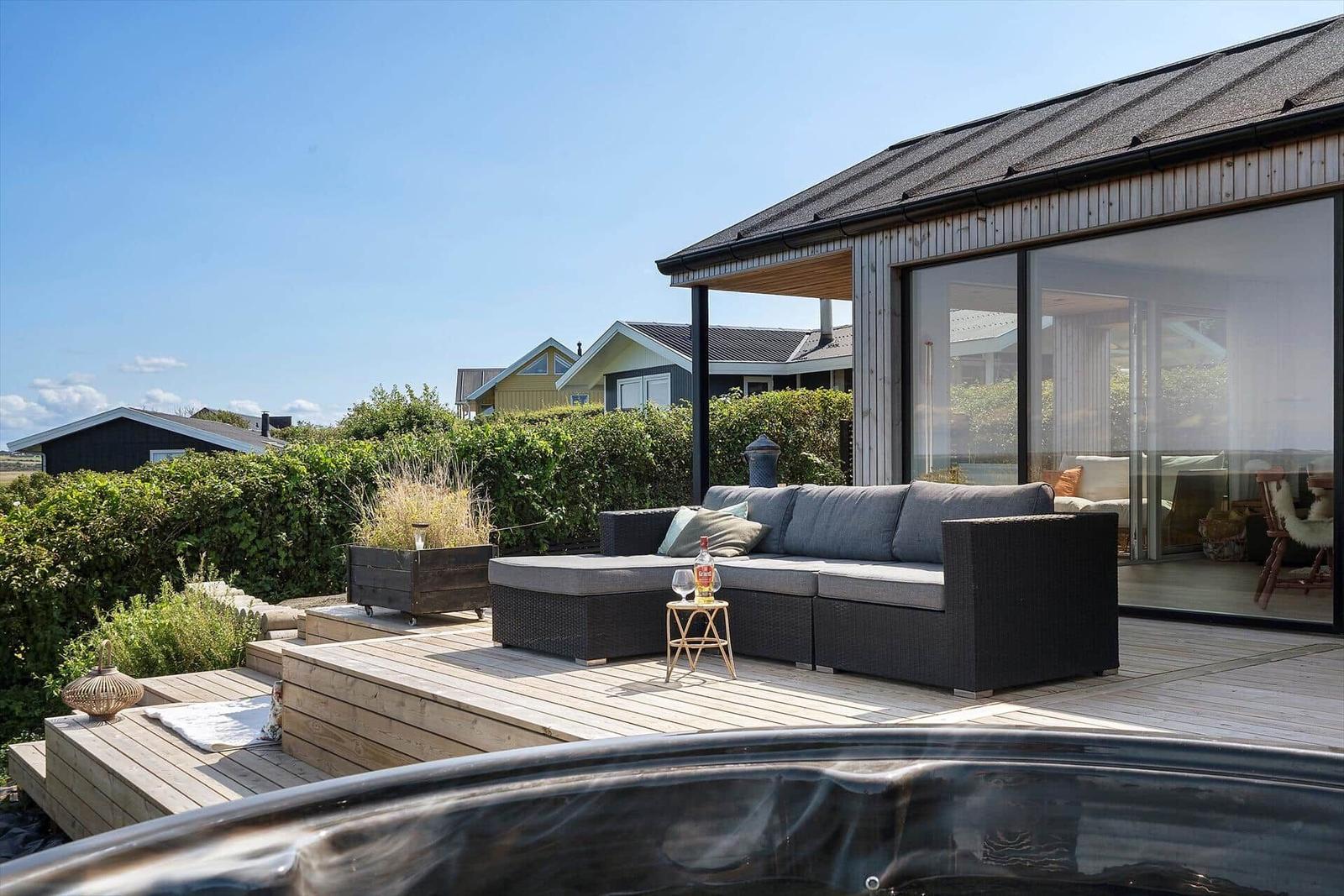 Terrasse mit Sitzgruppe und Whirlpool. Modernes Haus mit Glasfront und Holzverkleidung.