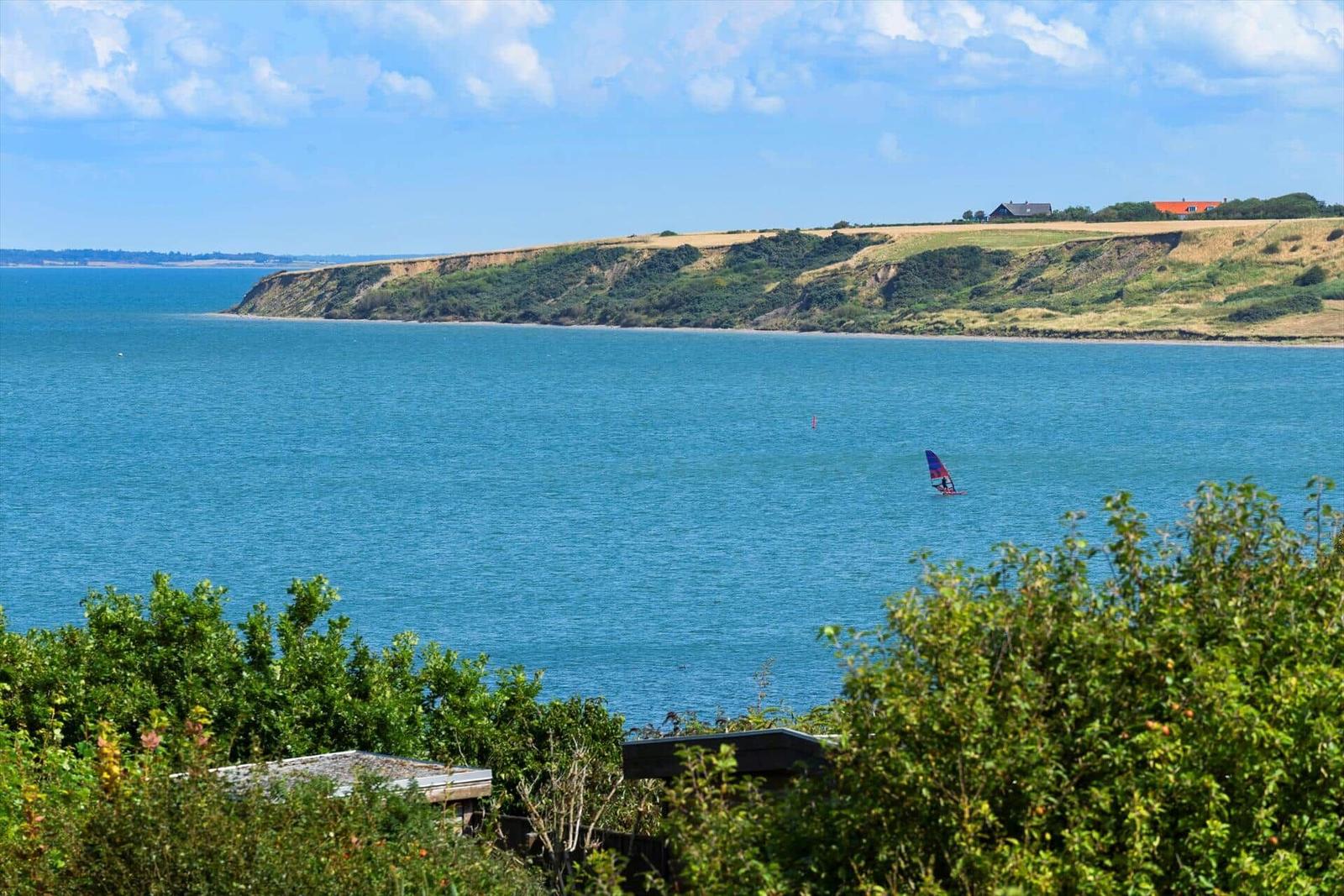 Meer mit Windsurfer und grüner Küstenlandschaft im Hintergrund.