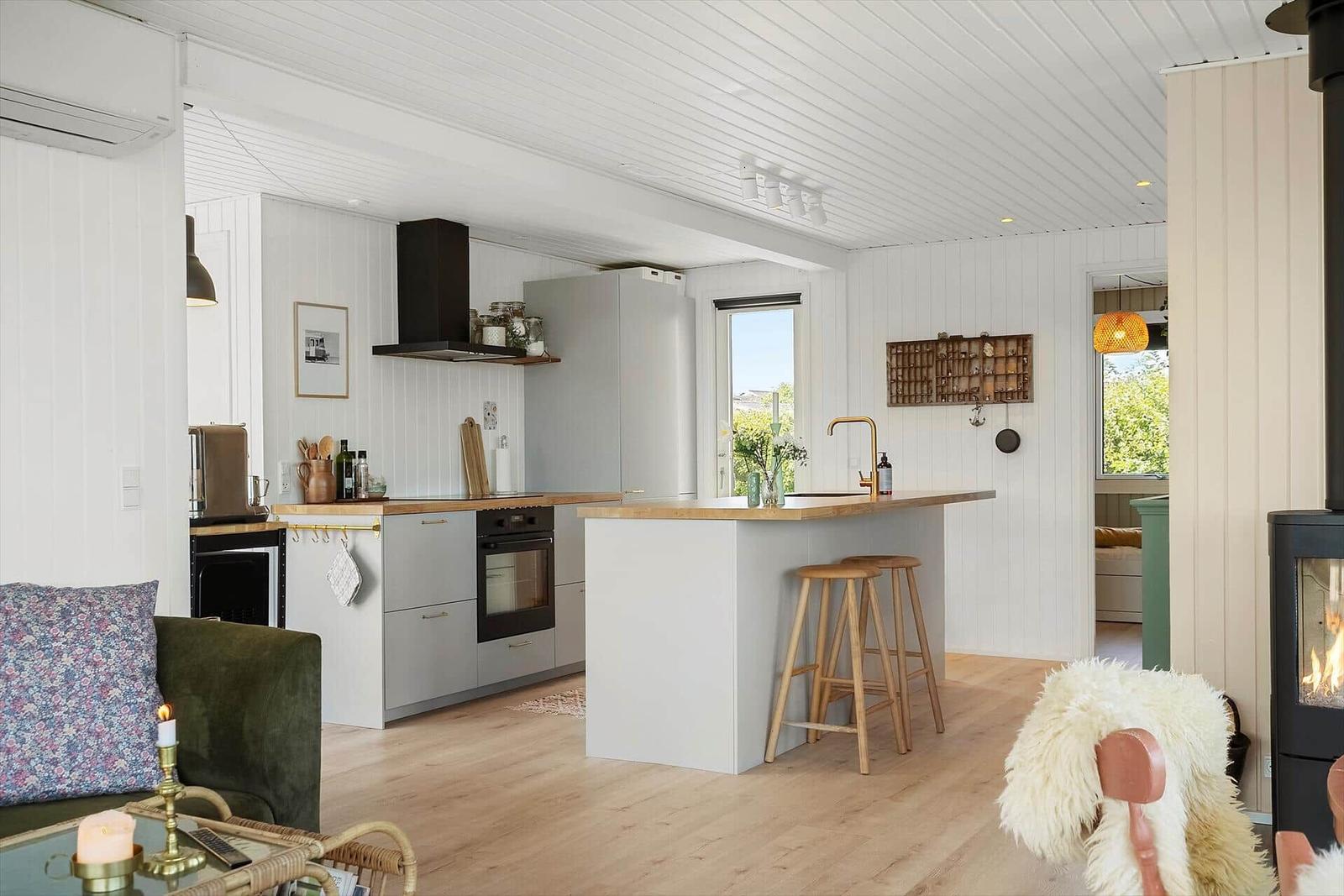 Küche mit Kücheninsel, Holzboden und weißen Wänden. Esstisch mit Stühlen und Kamin im Hintergrund.