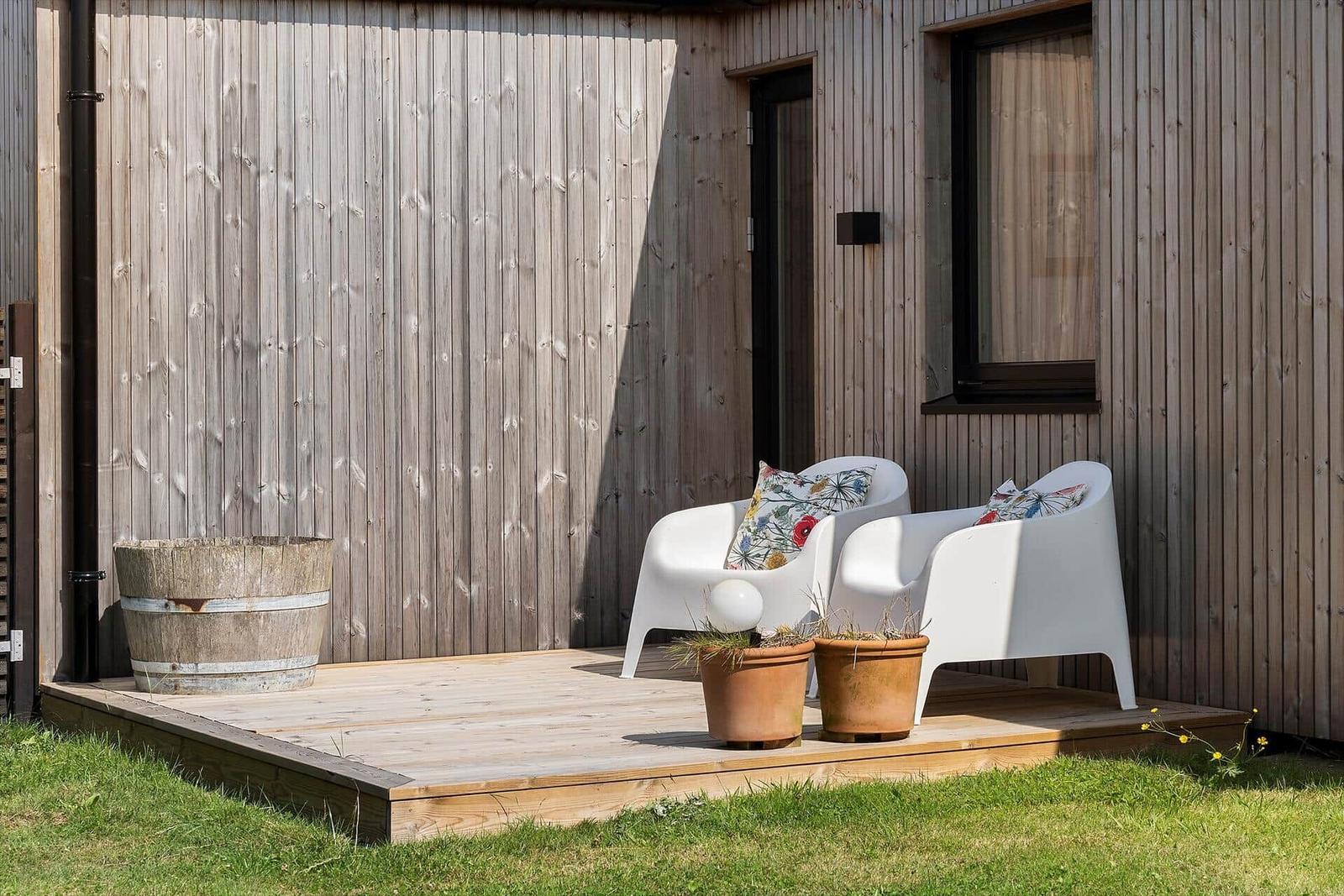 Terrasse mit zwei weißen Sesseln, Pflanzen und Holzwand.