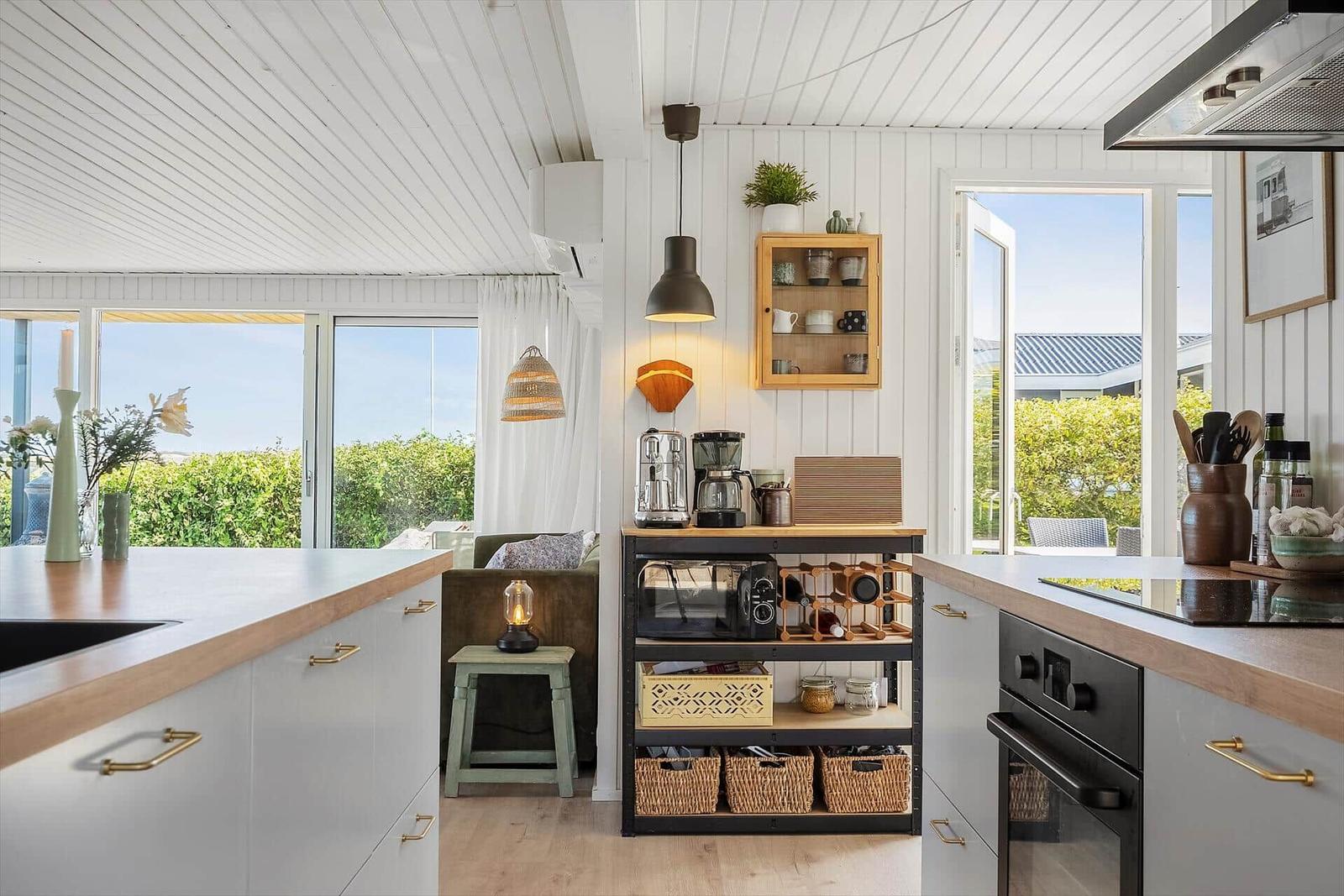 Küche mit hellen Wänden, Holzoberflächen und Blick auf grüne Außenbereiche.