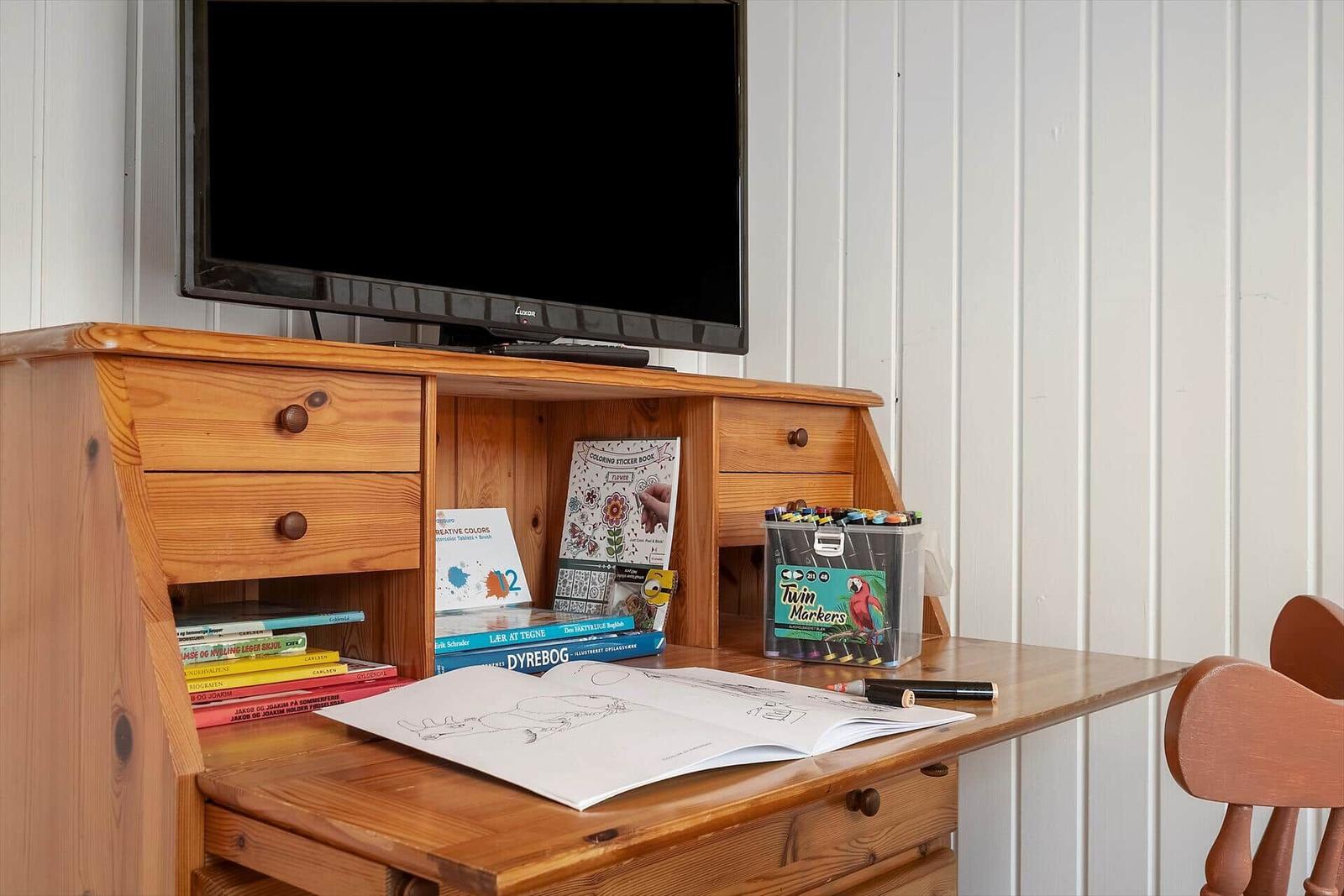 Holzschreibtisch mit Fernseher, Büchern und Malutensilien.