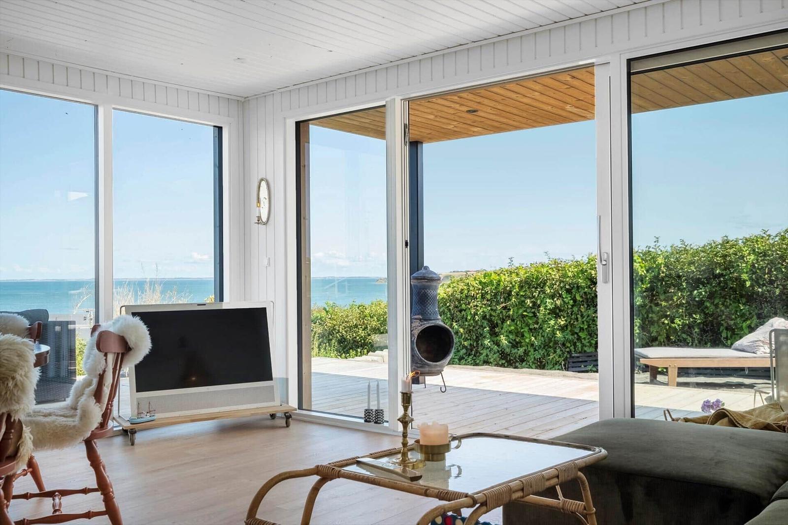 Wohnzimmer mit Meerblick, Fernseher und Terrasse mit Liegestuhl.