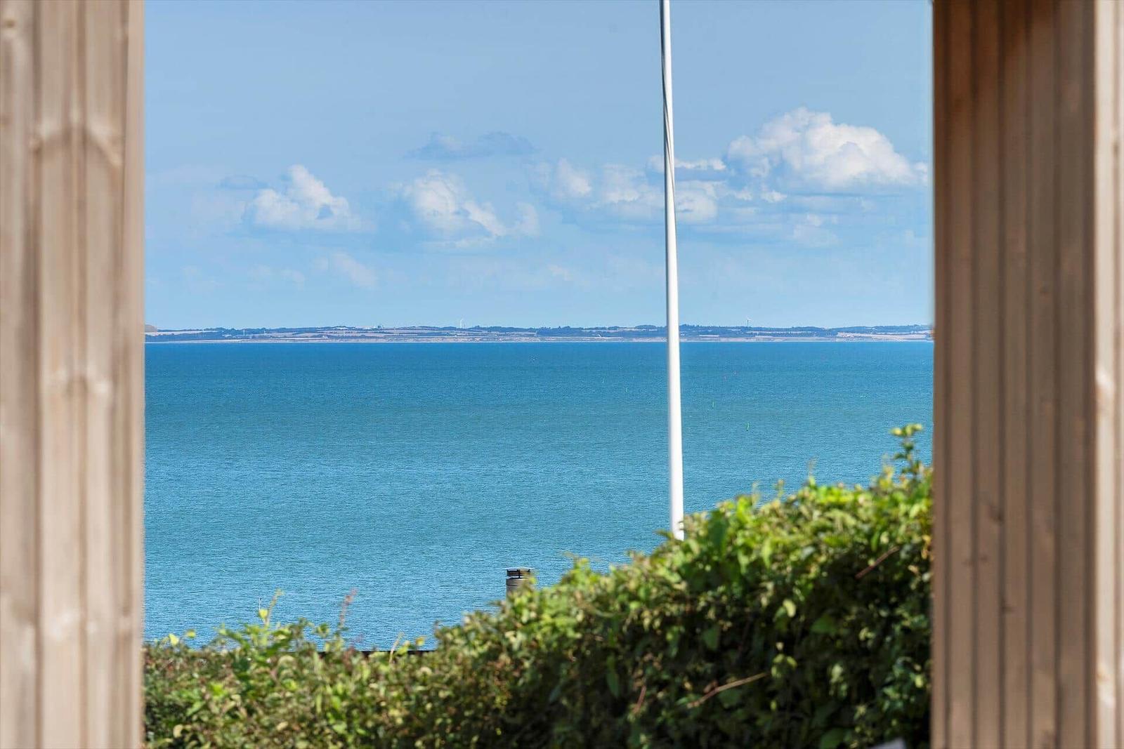 Blick durch Fenster auf tiefblaues Meer und Himmel mit Wolken.