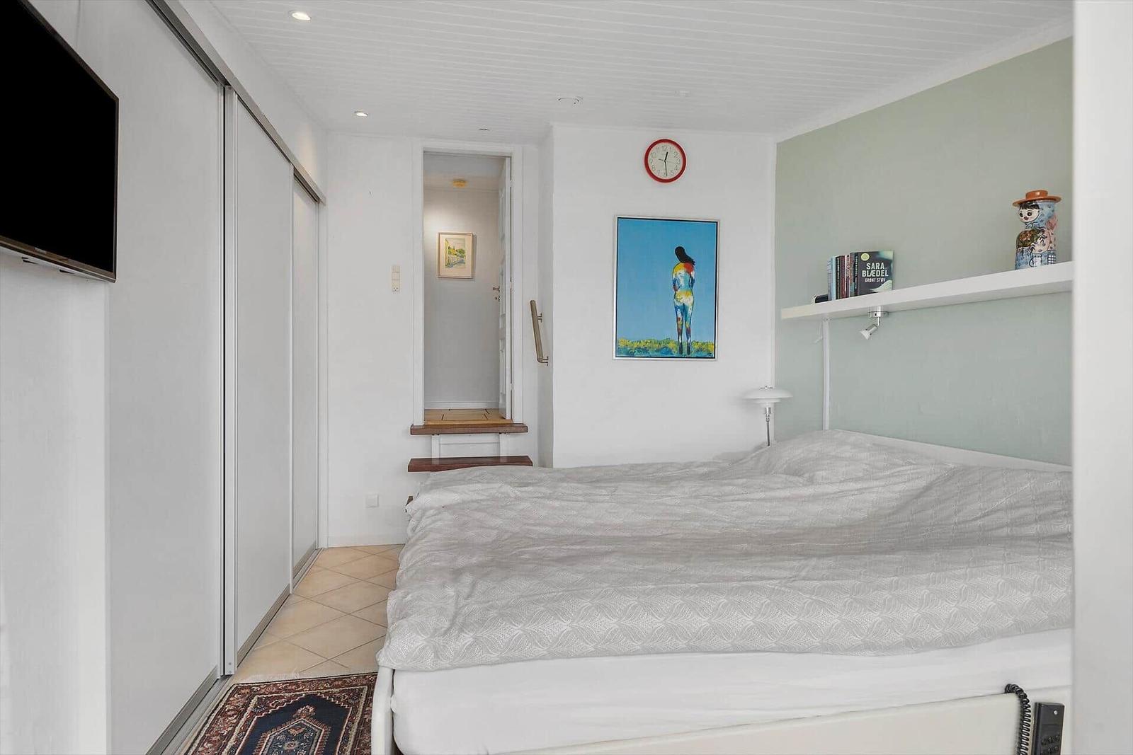 Schlafzimmer mit Bett, Wanduhr, Bild und Schwebetisch.