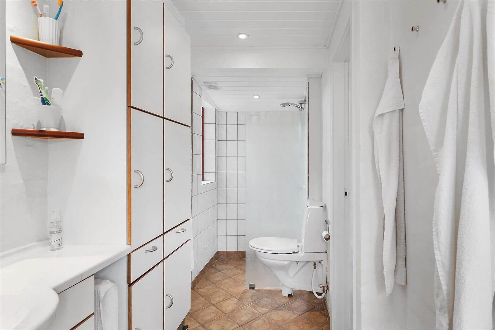 Badezimmer mit Dusche, Toilette und Waschbecken mit Schränken.