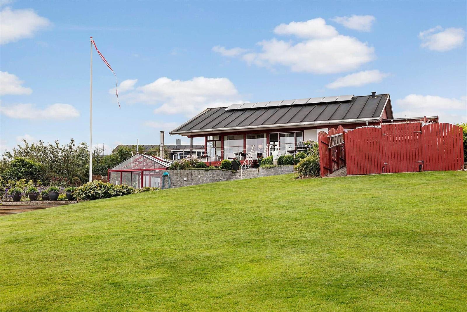 Rotes Haus mit Solaranlage und großem Garten unter blauem Himmel.