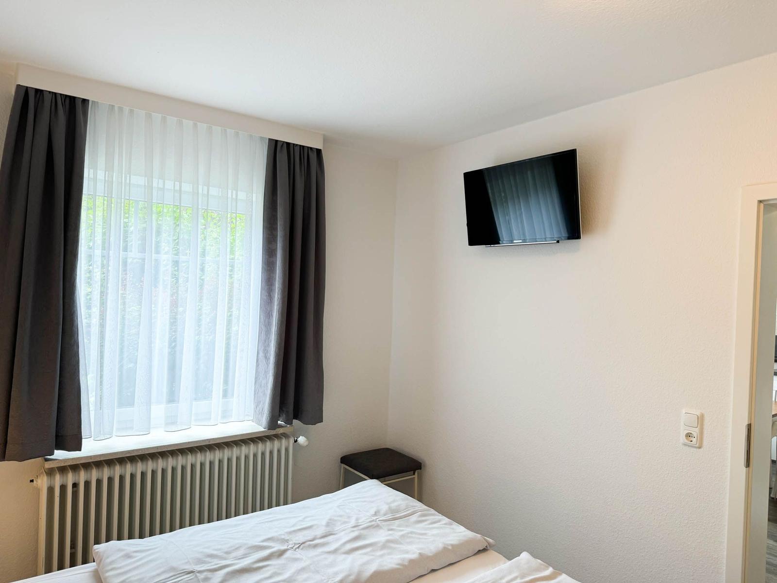 Zimmer mit Bett, TV und Fenster mit Vorhängen.