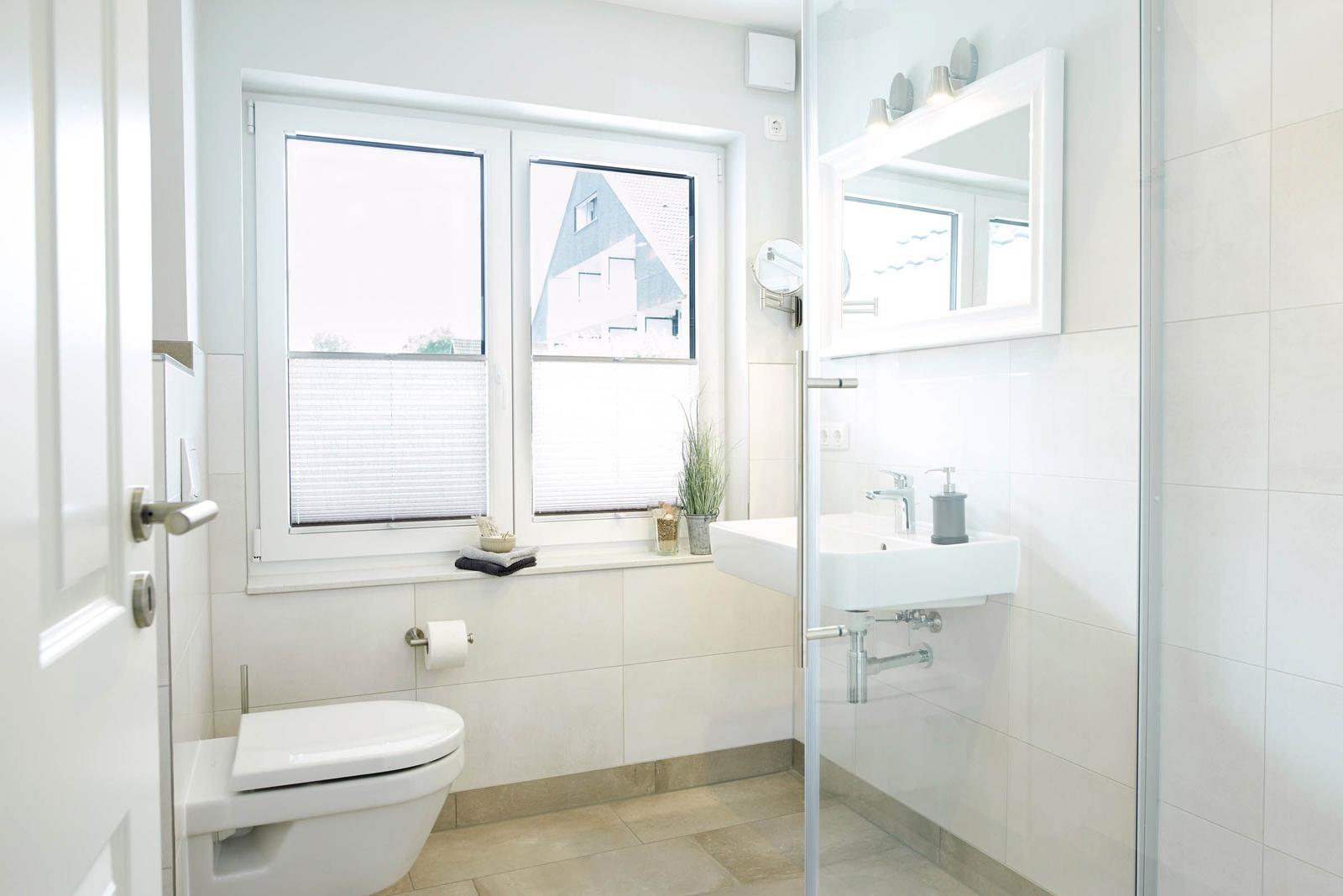 Badezimmer mit Toilette, Waschbecken und Dusche. Fenster mit Jalousie und Pflanze.