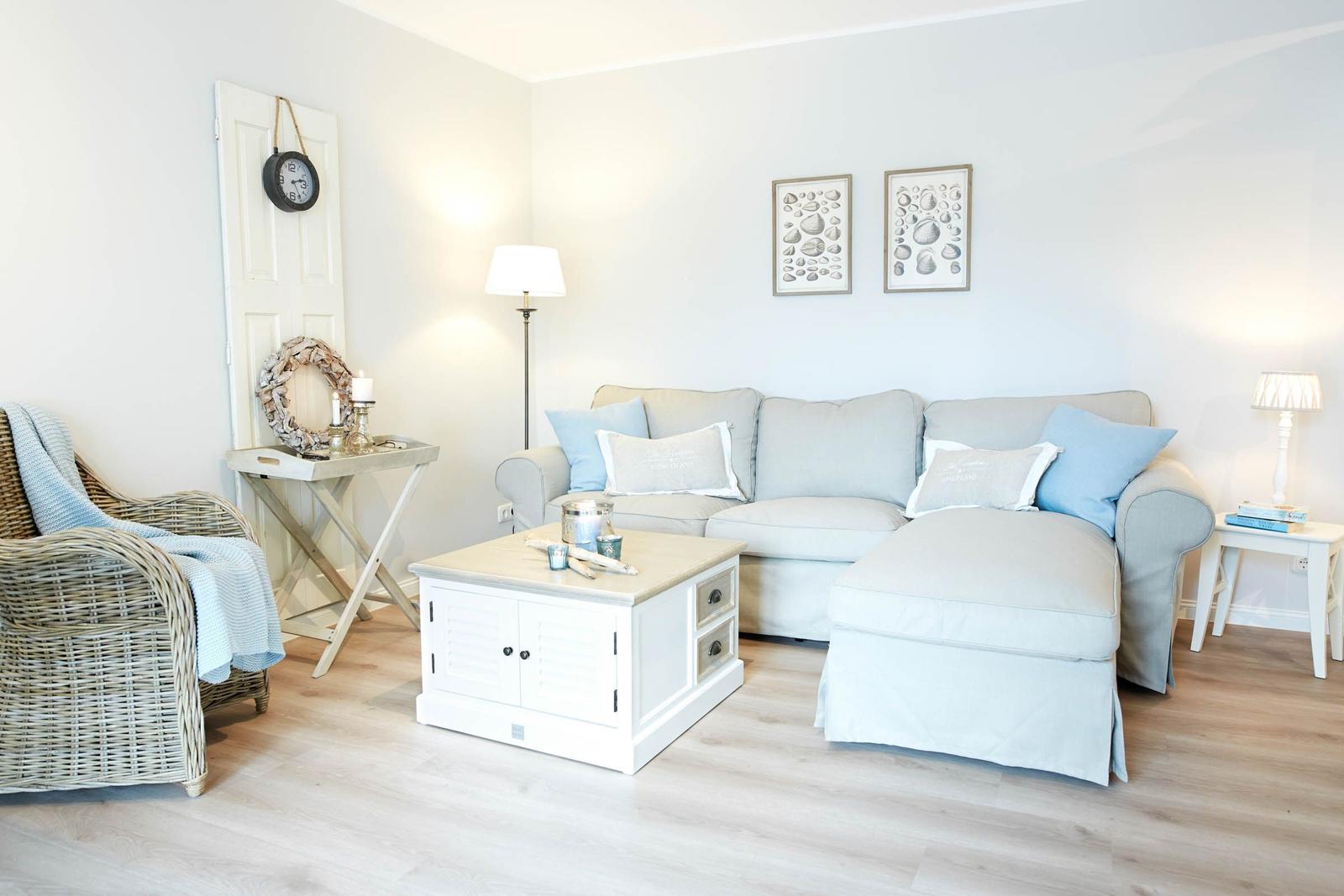 Wohnzimmer mit Sofa, Kaffeetisch und Sessel. Wandbilder und Stehlampe sind sichtbar.