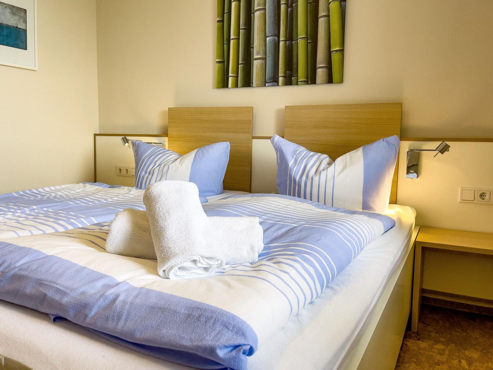 Doppelbett mit blau-weißem Bettzeug und aufgerollten Handtüchern.