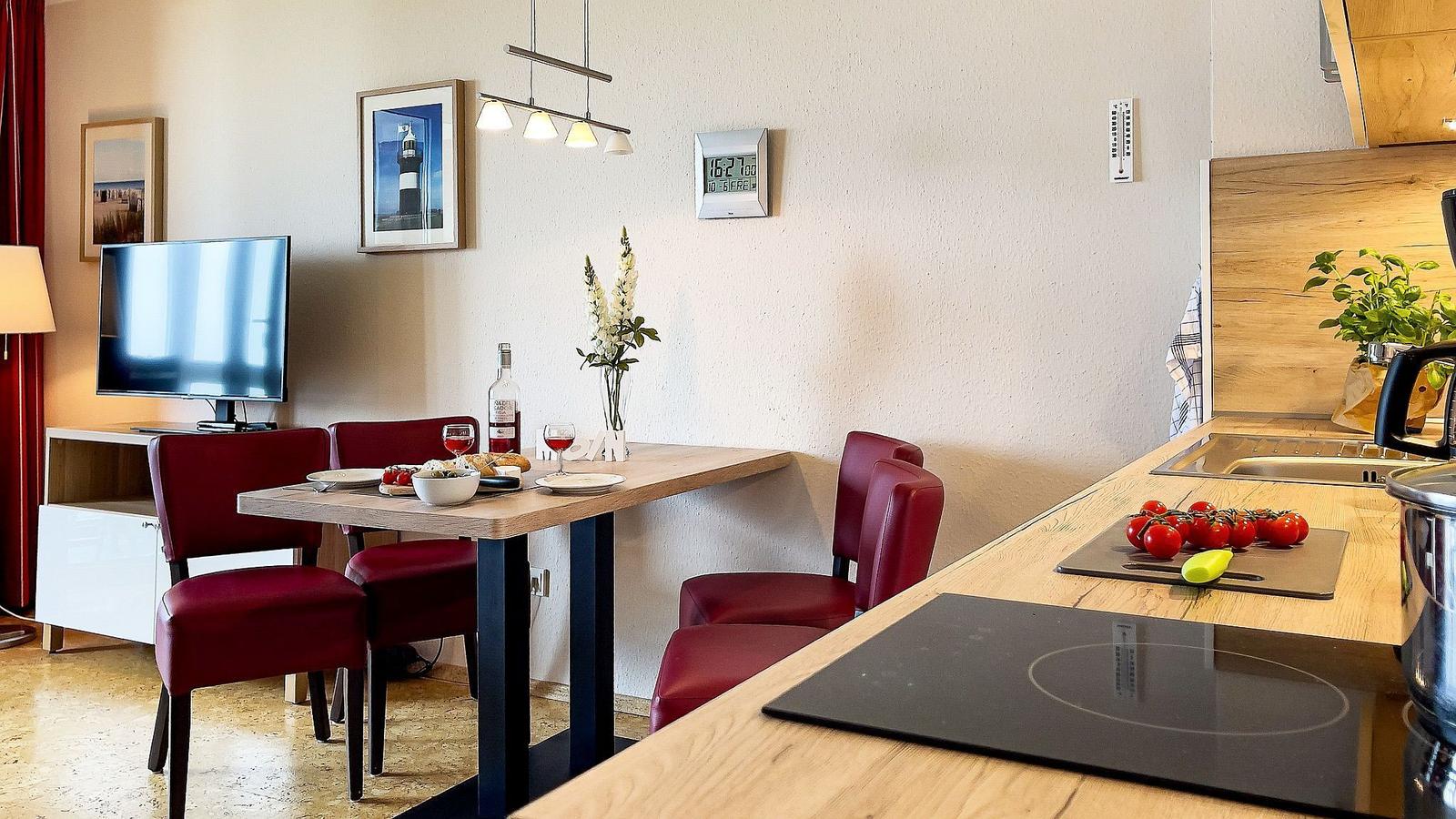 Essbereich mit Tisch, Stühlen und Küchenzeile. Wanduhr und Bilder an der Wand.