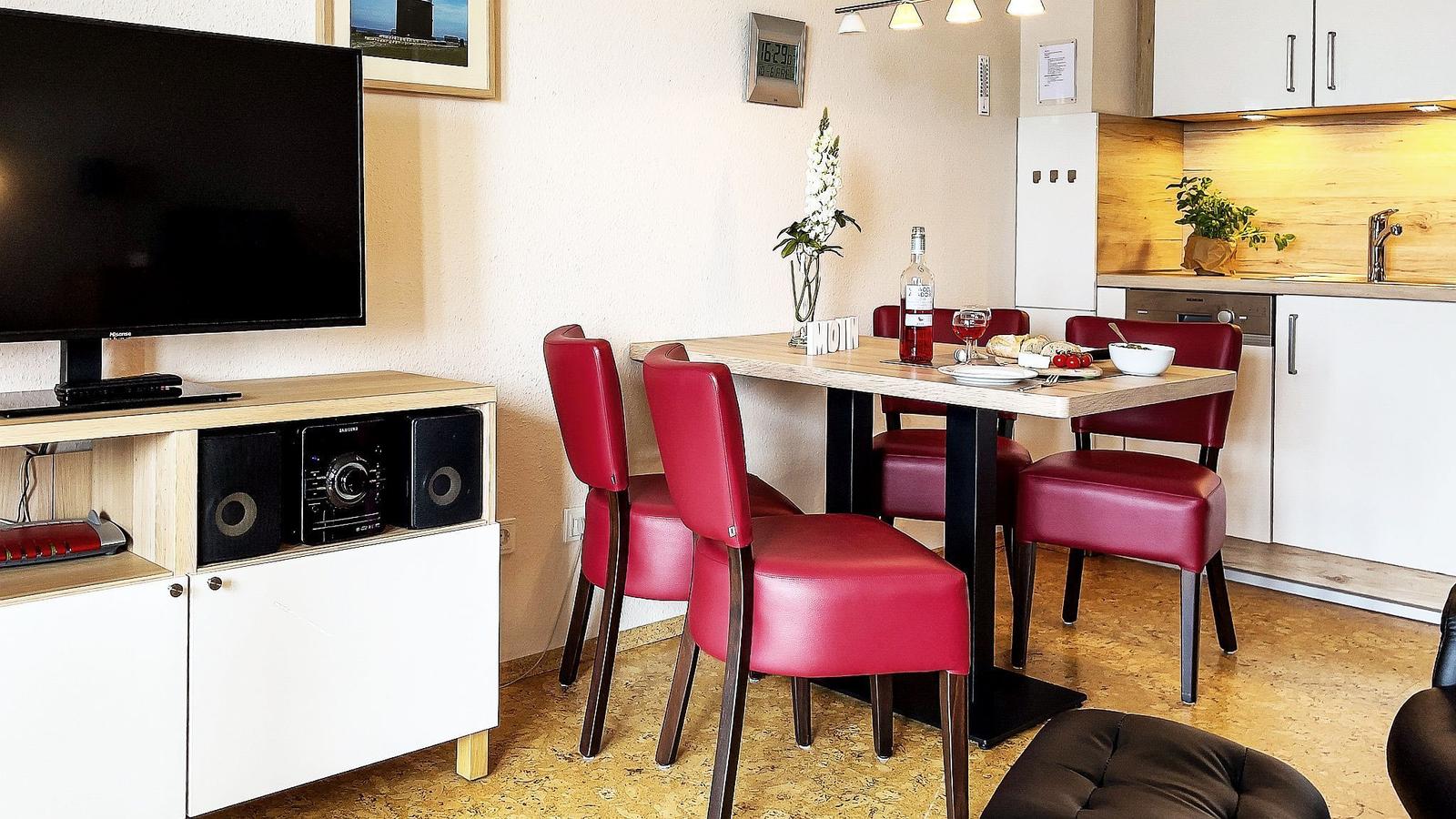 Essbereich mit roten Stühlen und Tisch. Küche mit Holzrückwand. Fernseher und Audioanlage.