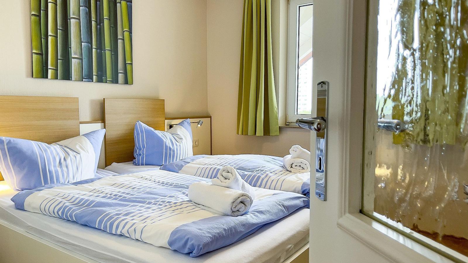 Zweibettzimmer mit blau-weißen Bettwäsche und grünen Vorhängen.