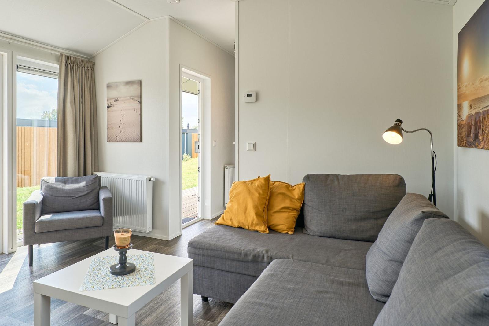 Wohnzimmer mit Sofa, Sessel und Tisch. Anblick auf Terrasse und Garten.