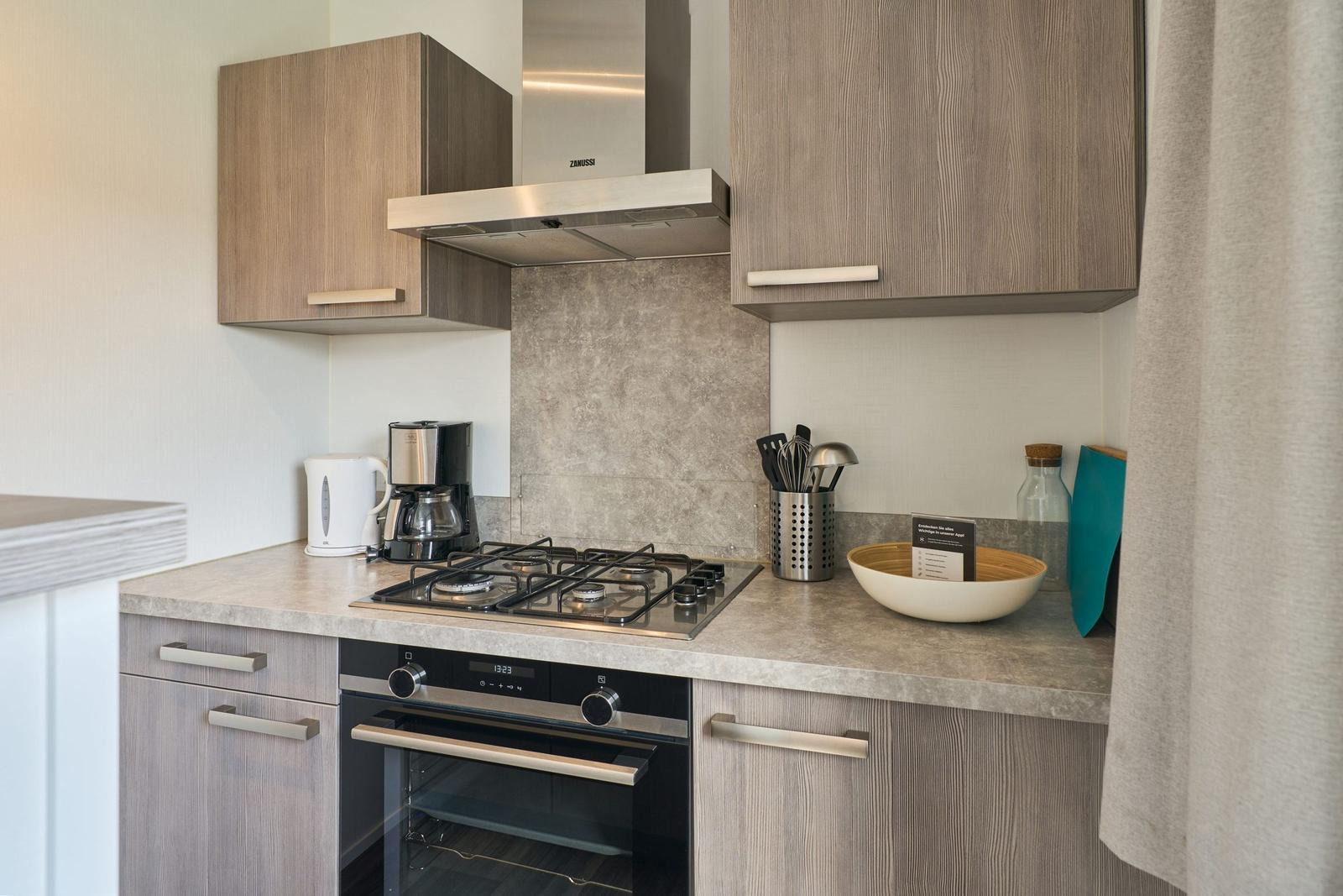 Küche mit Dunstabzugshaube, Herd und Backofen sowie Küchenutensilien.