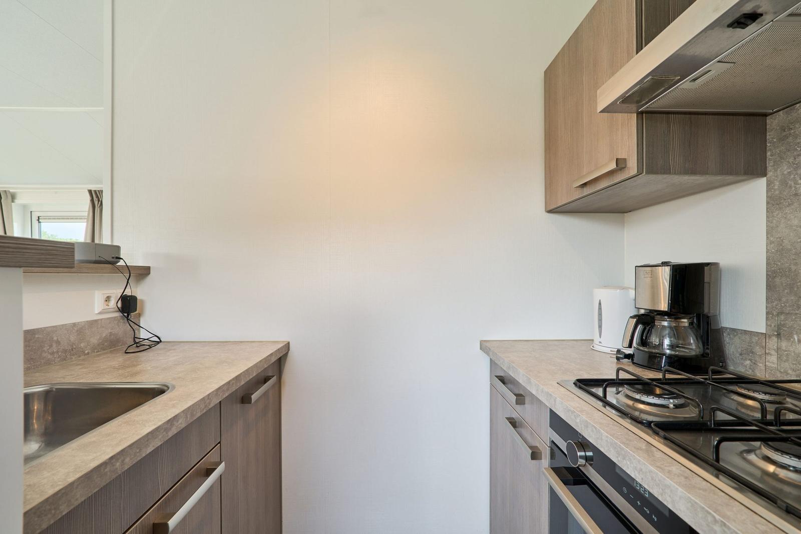 Küche mit Spüle, Kochfeld, Kaffeemaschine und Schränken.