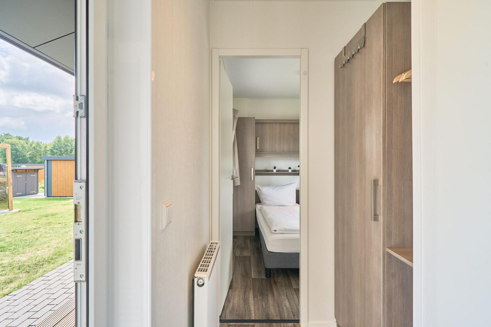 Schlafzimmer mit Bett und Kleiderschrank. Durchgang zur Terrasse mit Blick auf Garten.