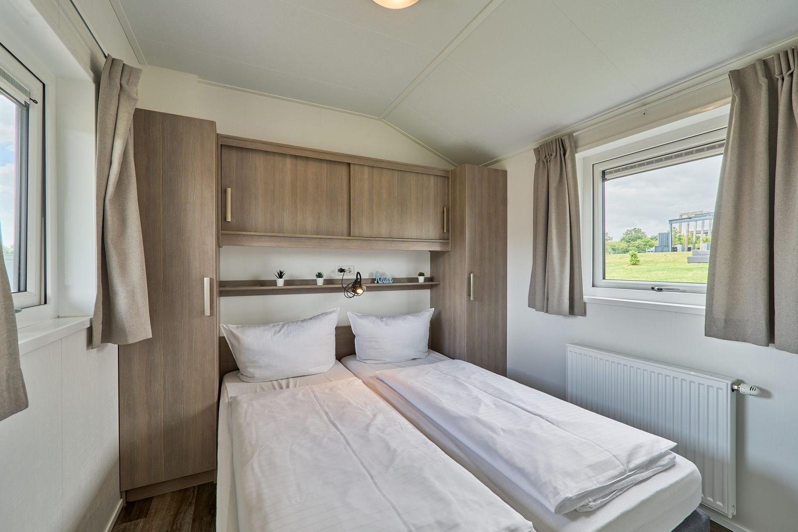 Zwei Einzelbetten mit weißen Bettwäsche, Holzmöbel und Fenster mit Blick auf Grünfläche.