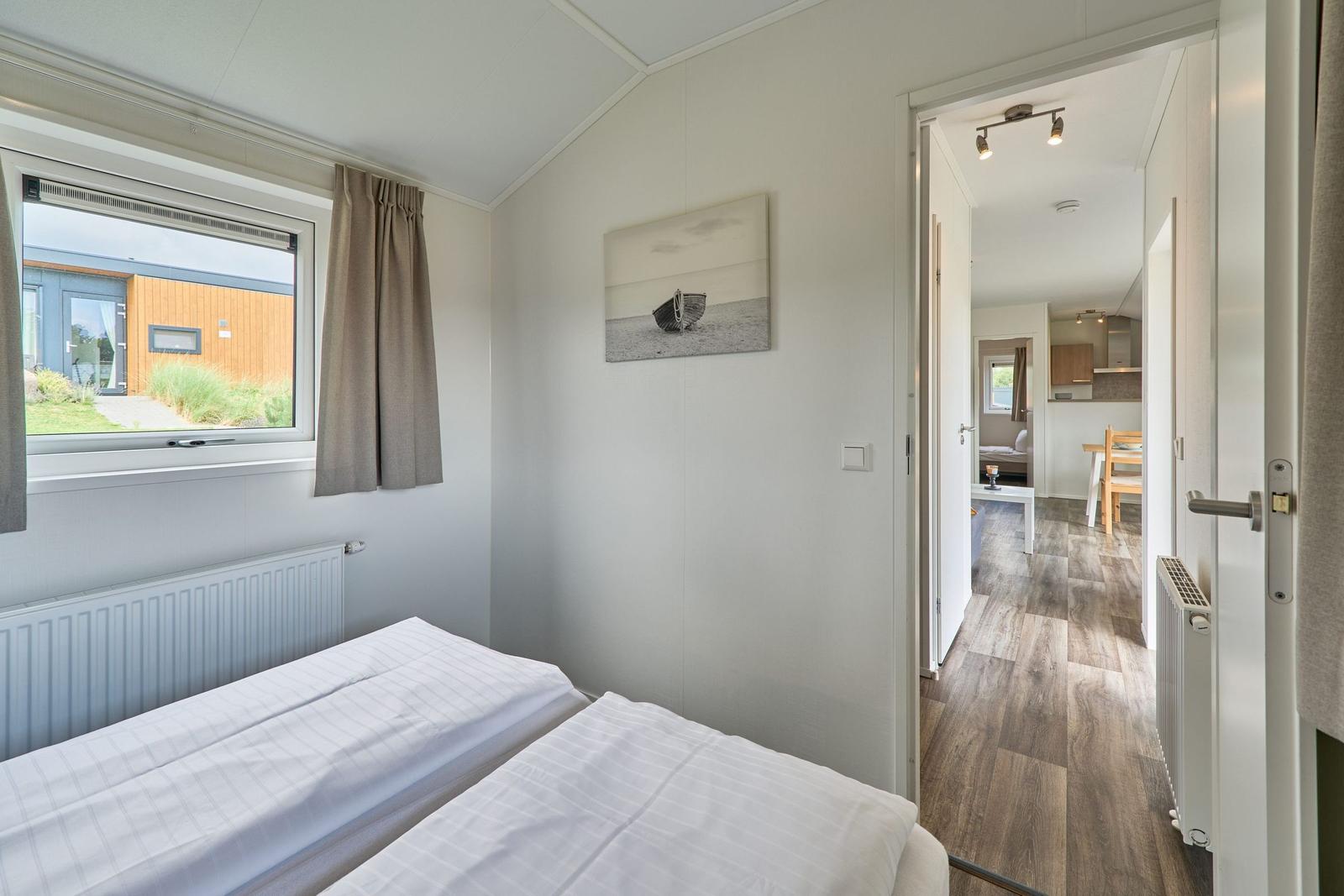 Schlafzimmer mit Bett, Fenster und Blick in die Küche.