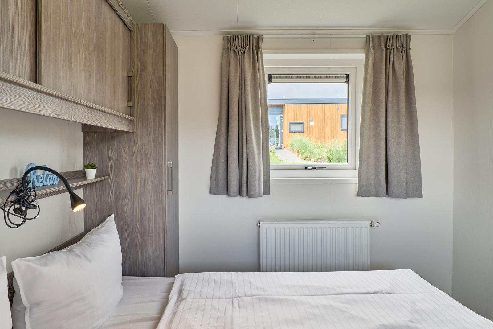 Schlafzimmer mit Bett, Schrank und Fenster mit Blick auf Außenbereich.