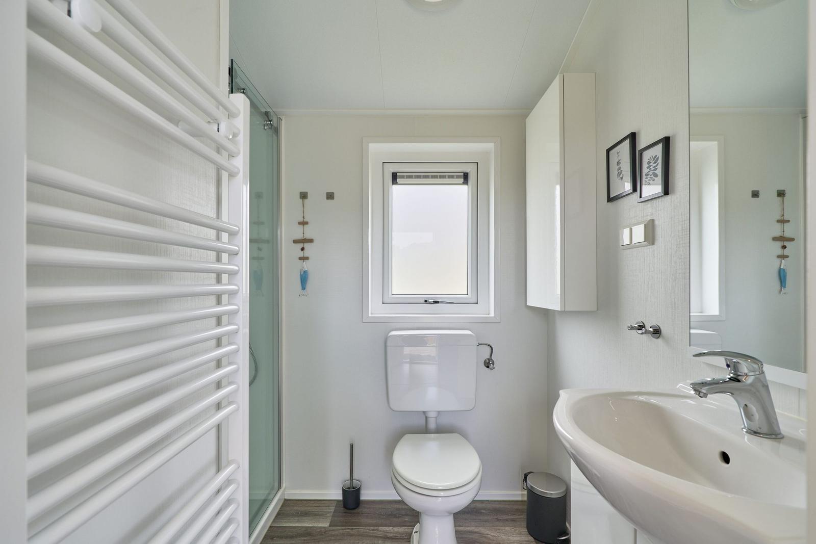 Badezimmer mit Dusche, Toilette und Waschbecken. Fenster und Spiegel sichtbar.