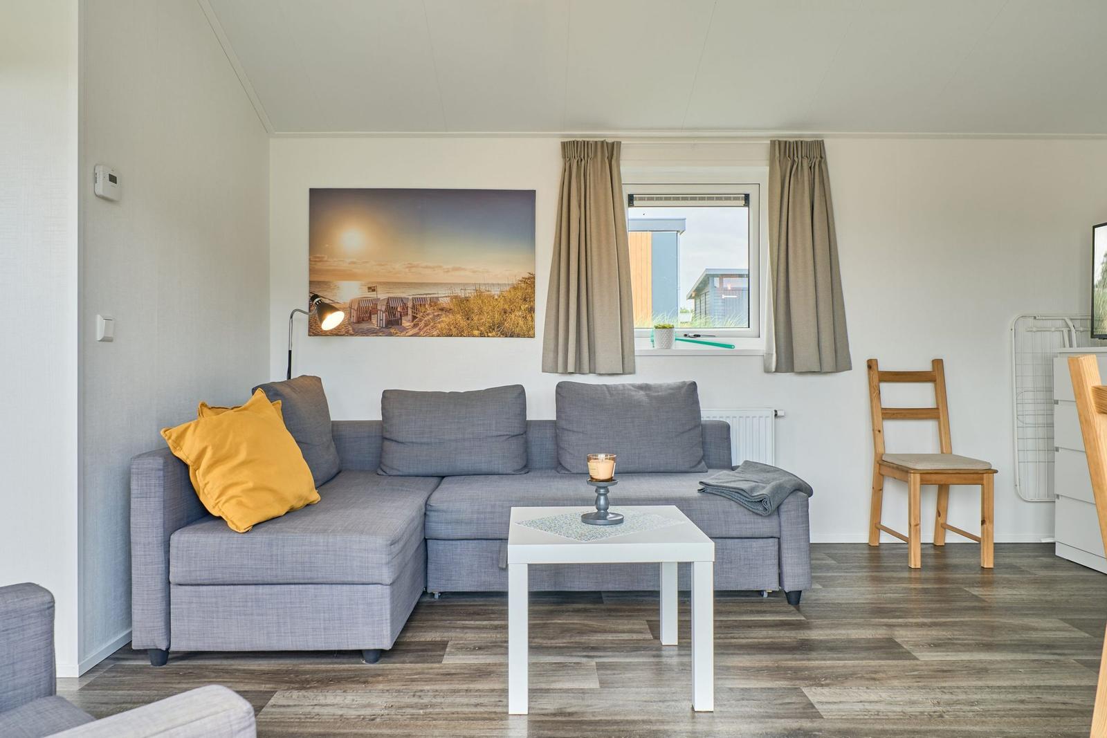 Wohnzimmer mit grauem Sofa, Holzboden und Fenster mit Blick.