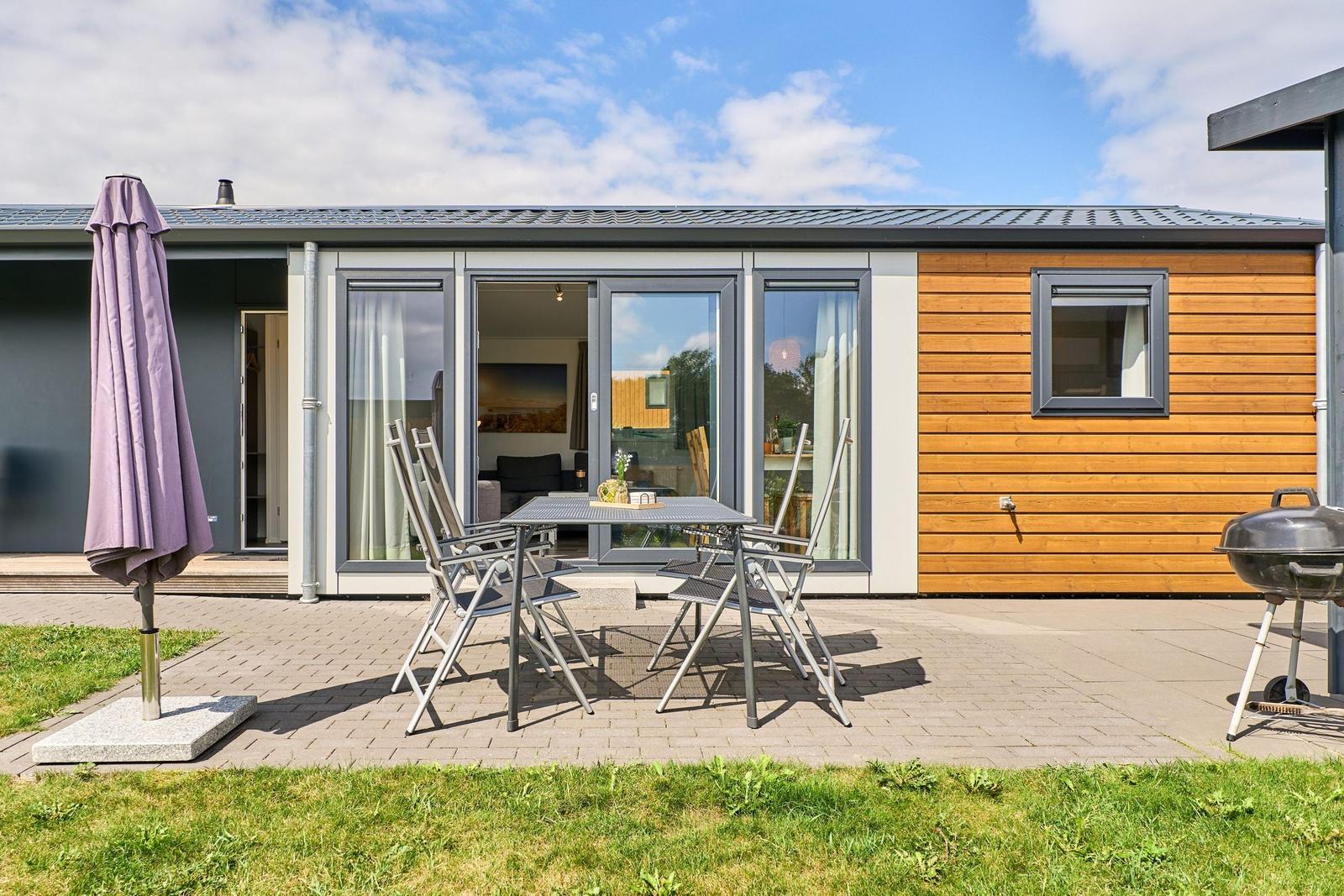 Terrasse mit Tisch, Stühlen, Sonnenschirm und Grill. Durchgehende Glastüren zum Innenraum.