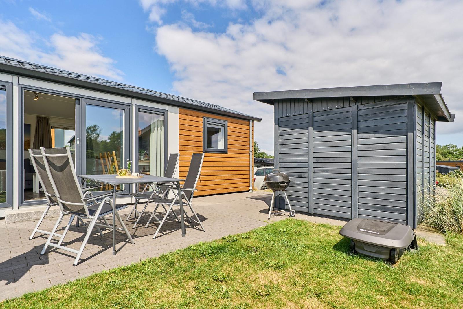 Terrasse mit Sitzgruppe, Grill und Gartenhaus neben modernem Ferienhaus.