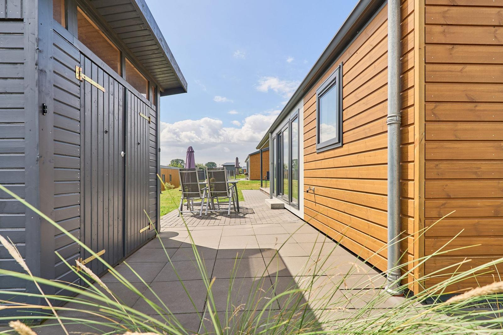 Terrasse mit Sitzgruppe zwischen Holzhäusern unter blauem Himmel.