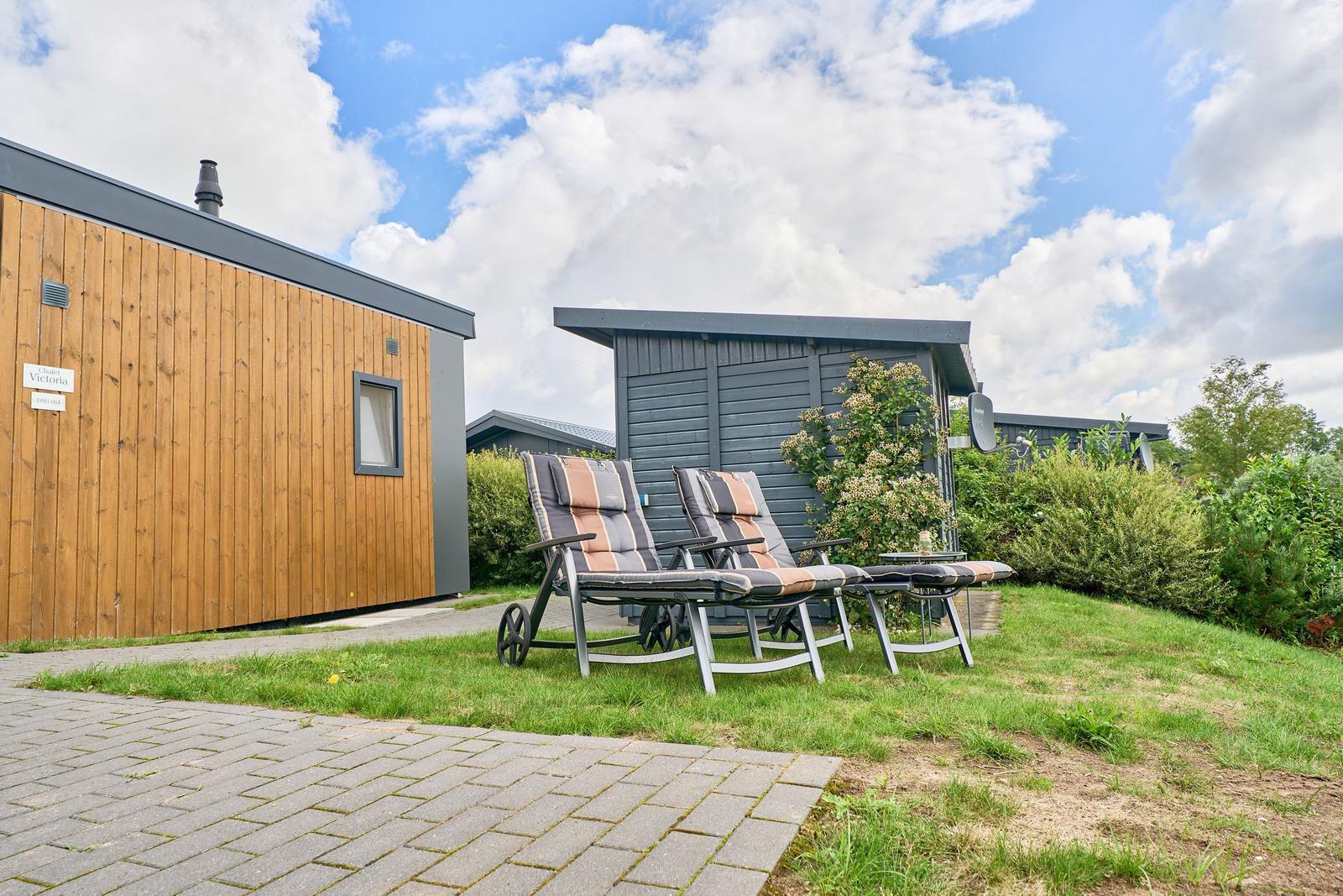 Zwei Liegestühle stehen auf einer Wiese vor einem Holzhaus mit grauem Dach.