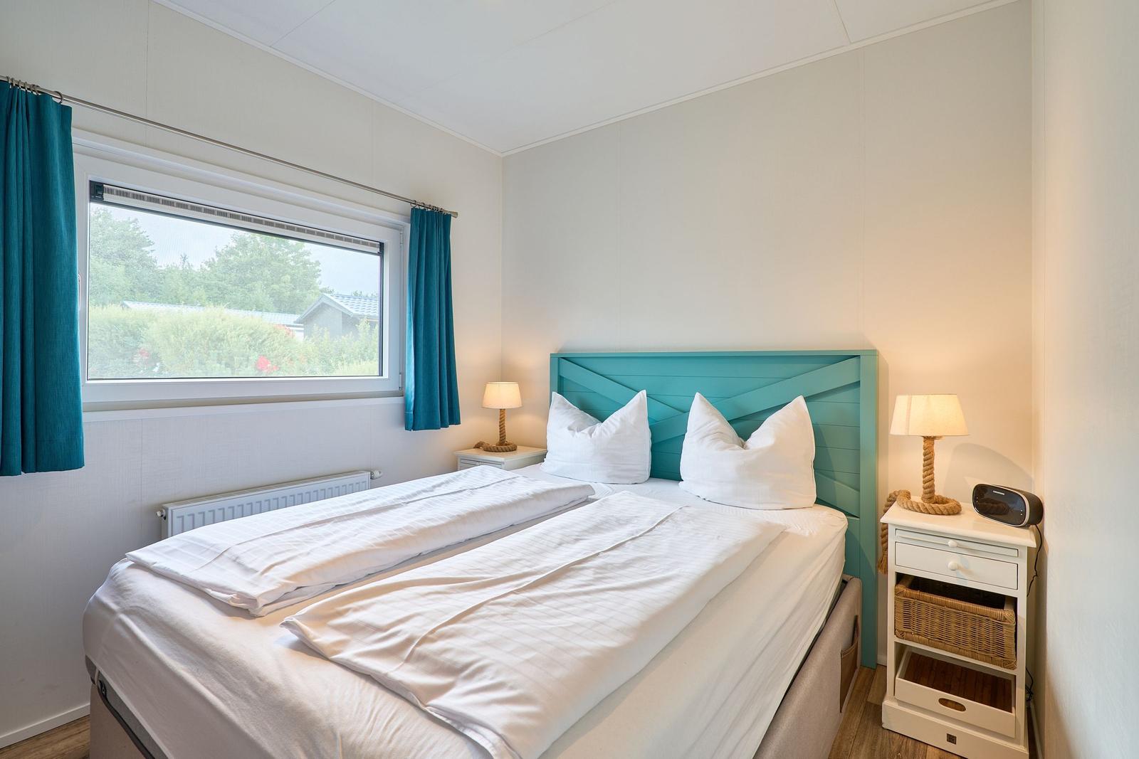 Schlafzimmer mit Bett, Nachttischen und Fenster mit Blick auf Grün.