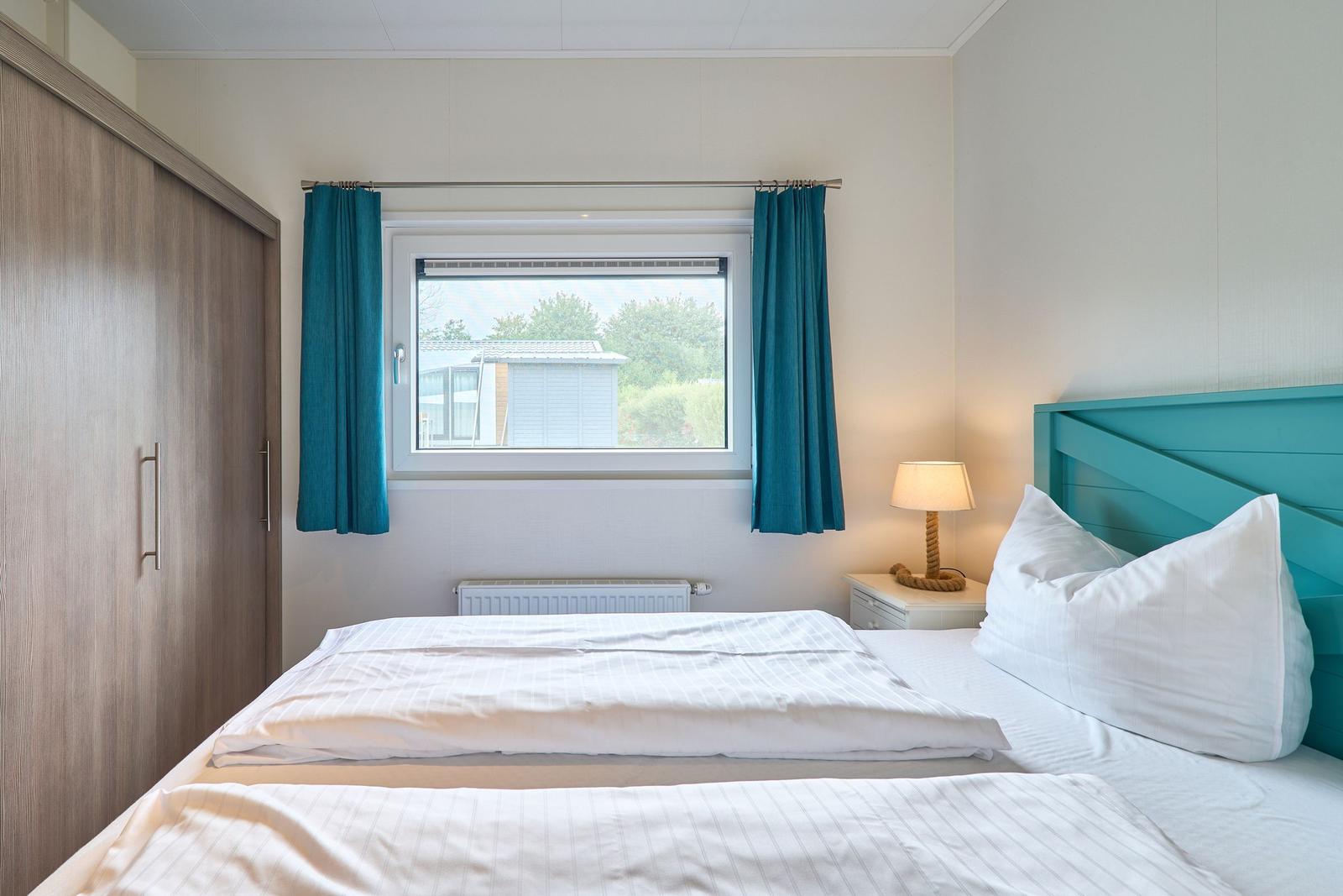 Schlafzimmer mit Bett, Nachttisch und Fenster mit Vorhängen.