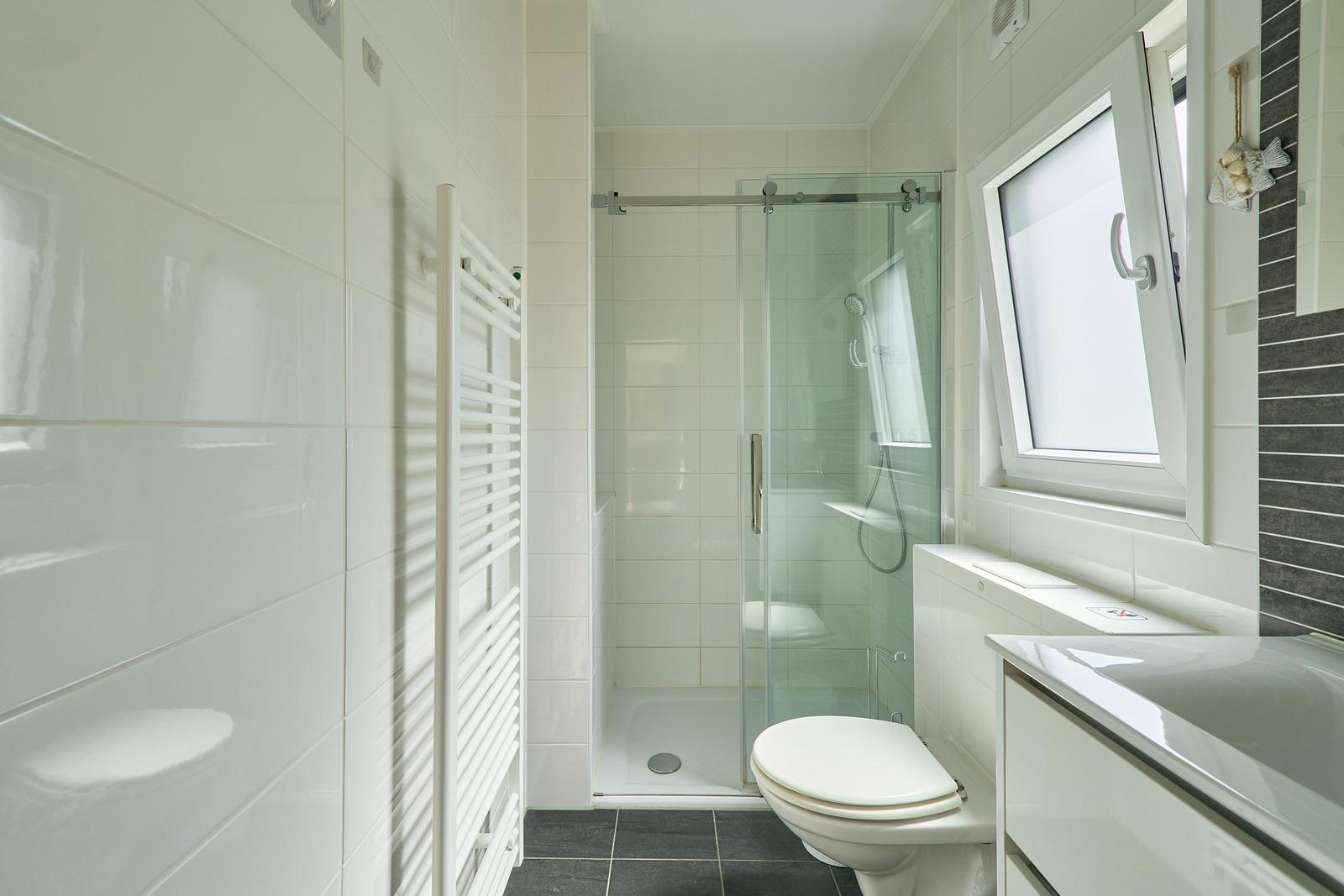 Badezimmer mit Dusche, Toilette und Waschbecken. Fenster und Heizung sind vorhanden.