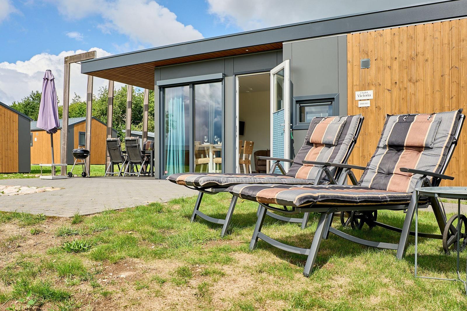 Zwei Liegestühle stehen auf dem Gras vor einem Chalet mit Terrasse und Grill.