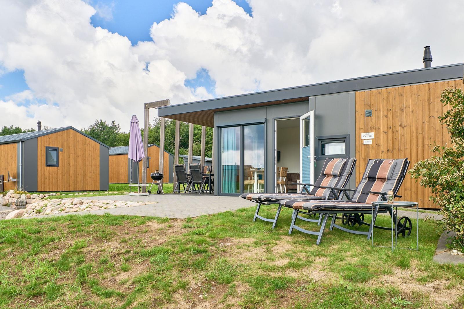 Moderne Ferienhaus mit Terrasse, Liegestühlen und Grillplatz im Grünen.