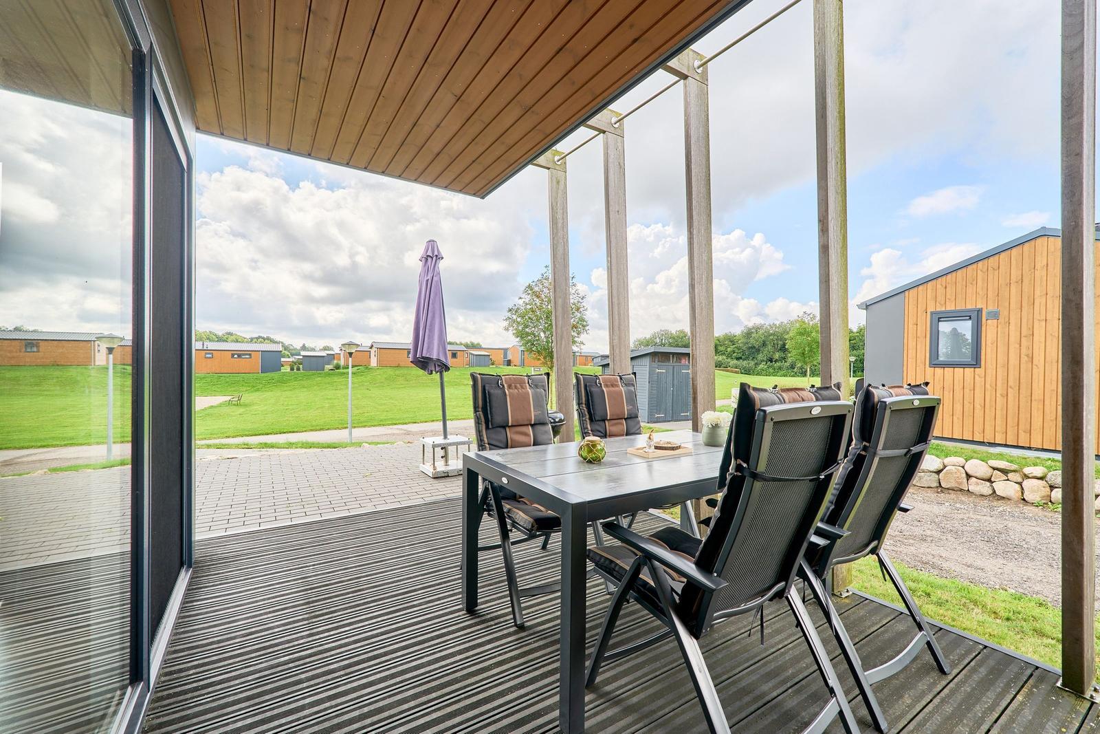 Terrasse mit Tisch und Stühlen, Blick auf grüne Wiesen und Holzhäuser.