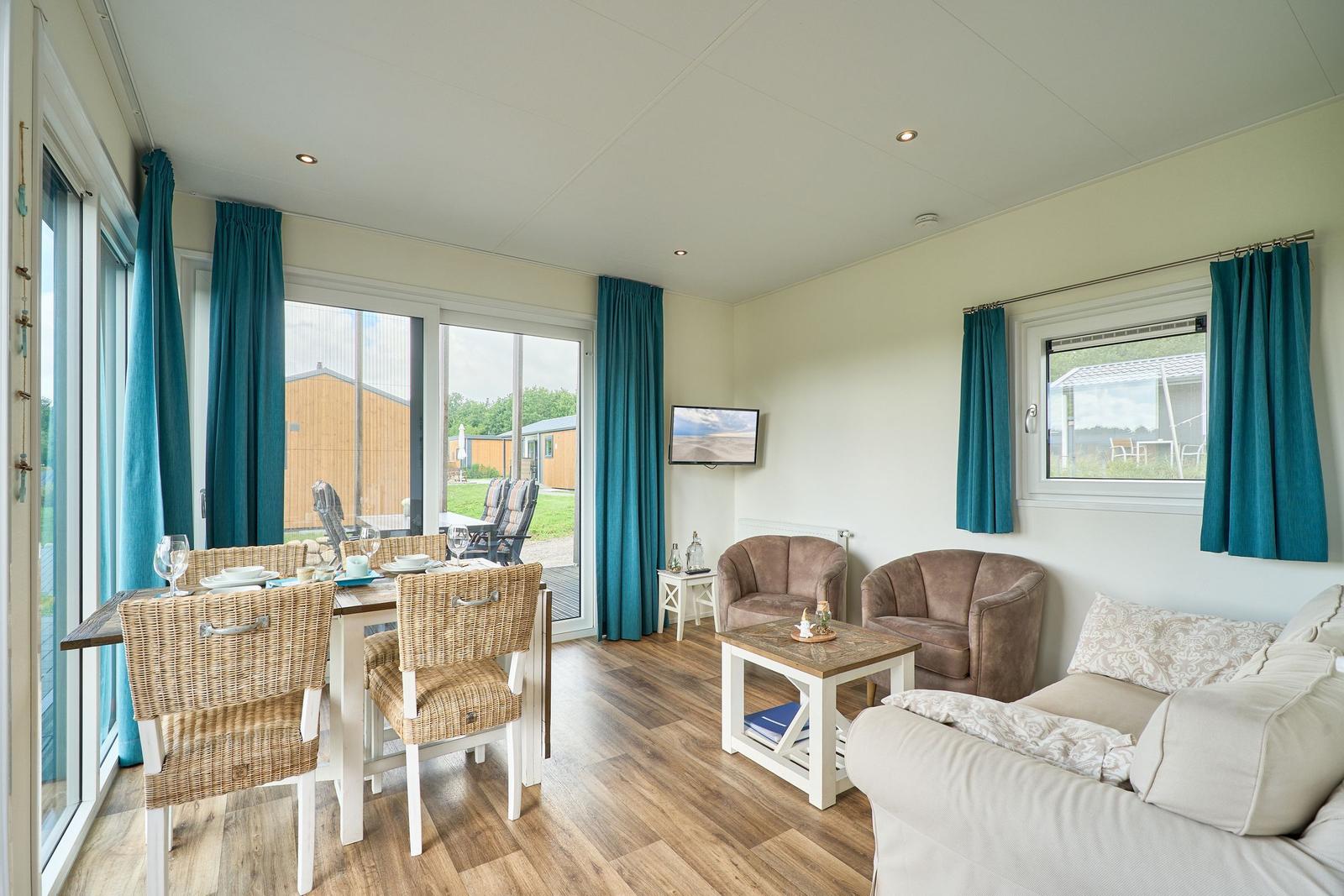 Wohn- und Essbereich mit Sofa, Stühlen und TV. Blick auf Garten.