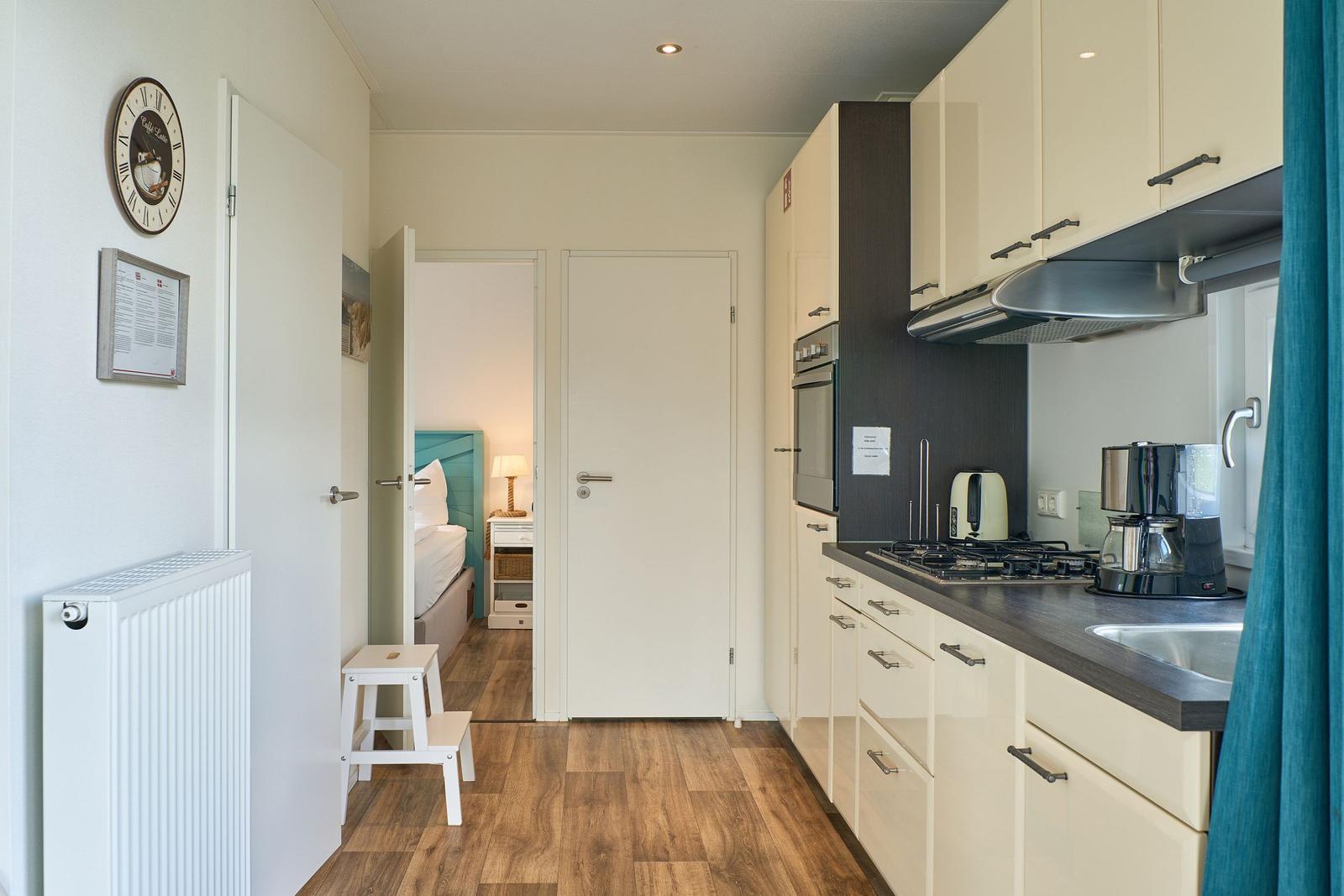 Küche mit Arbeitsfläche, Herd und Kaffeemaschine. Durchgang zu Schlafzimmer mit Bett.