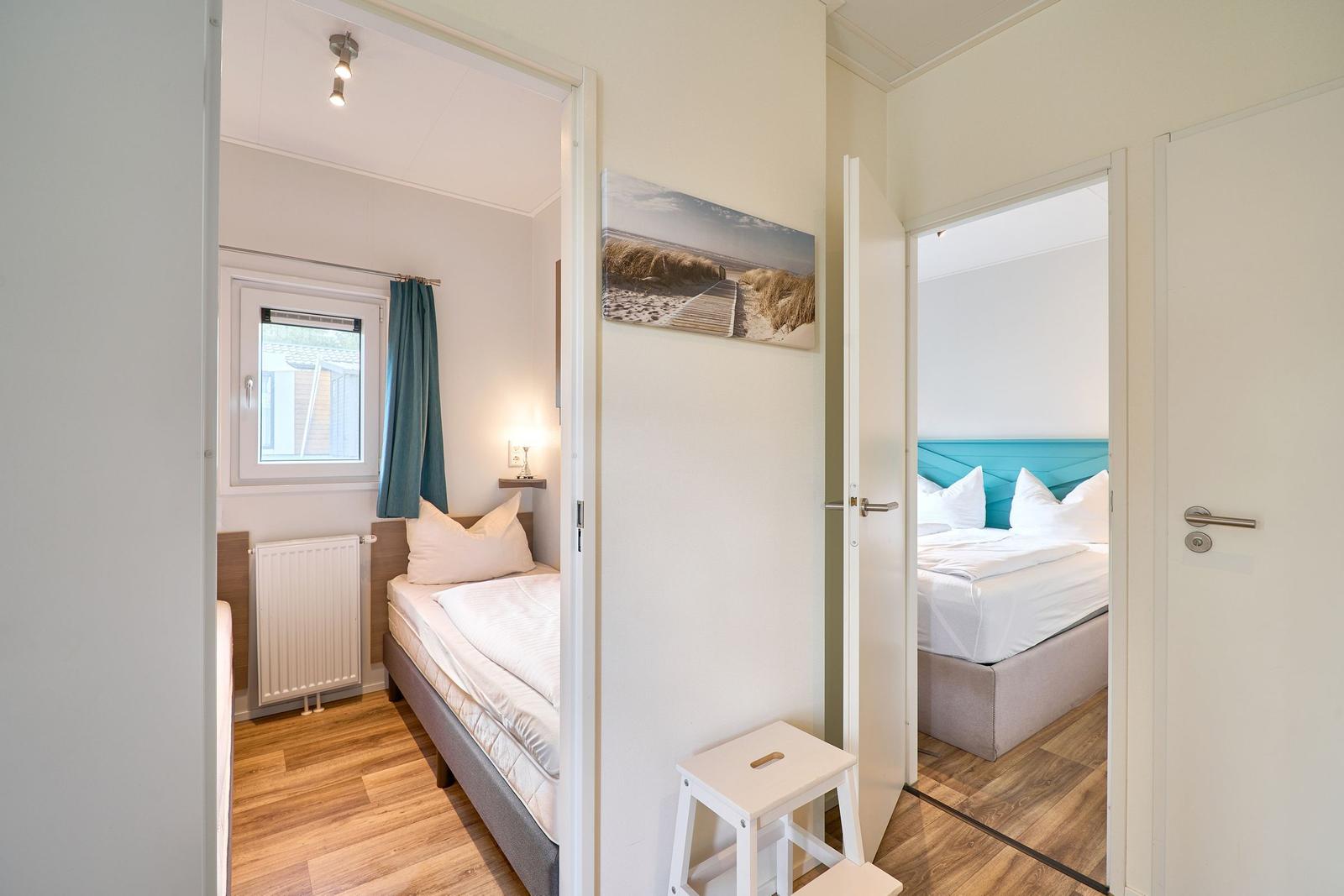 Zwei Schlafzimmer mit Betten, Fenster und Holzboden. Wandbild zeigt Strand.