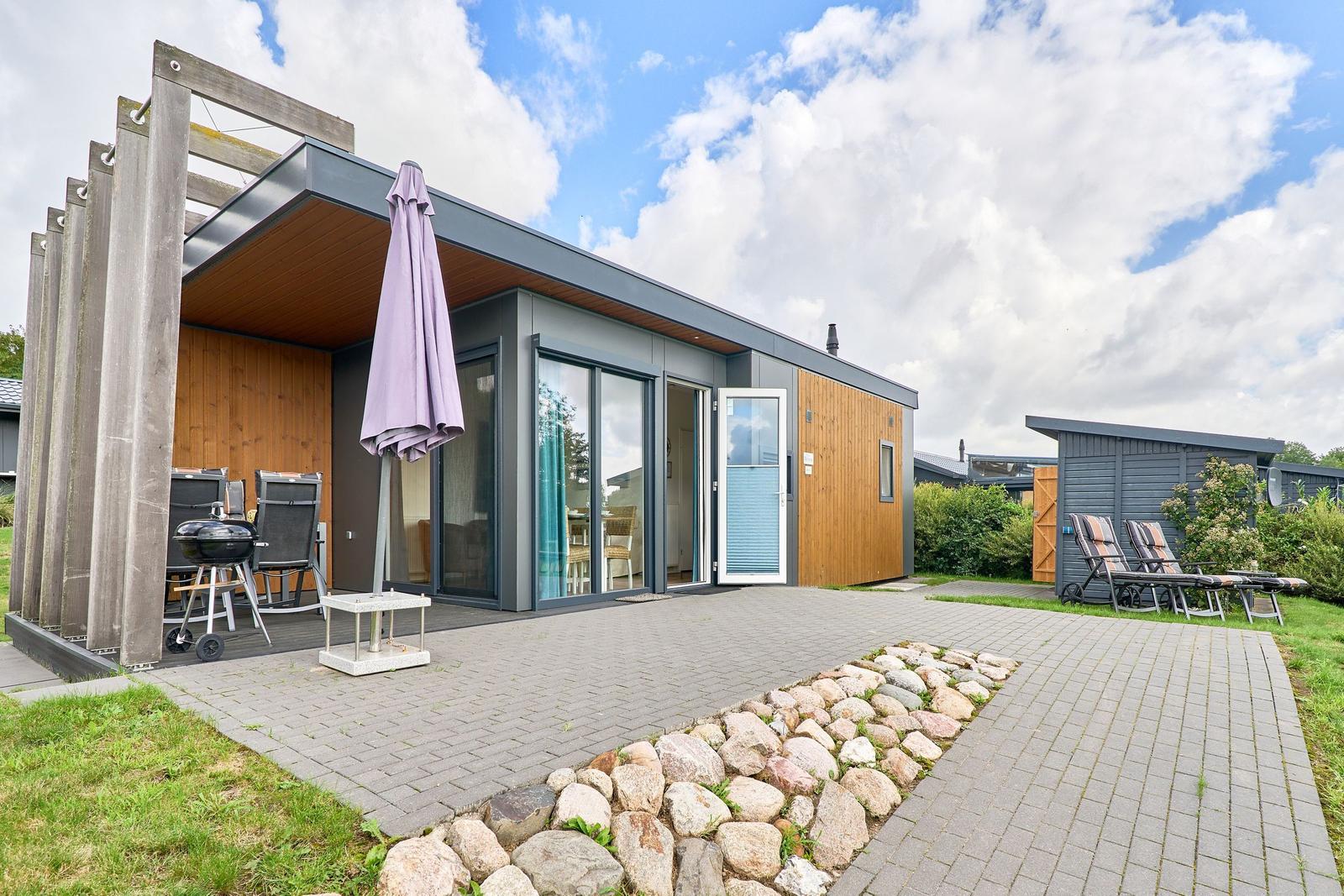 Moderne Ferienhaus mit Terrasse, Grill und Sonnenliegen im Garten.