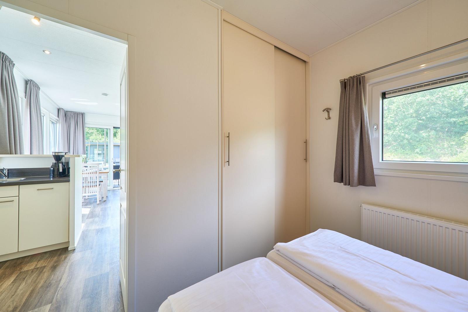 Zwei Betten, Schiebetürenschrank und Fenster mit Blick auf Wald.