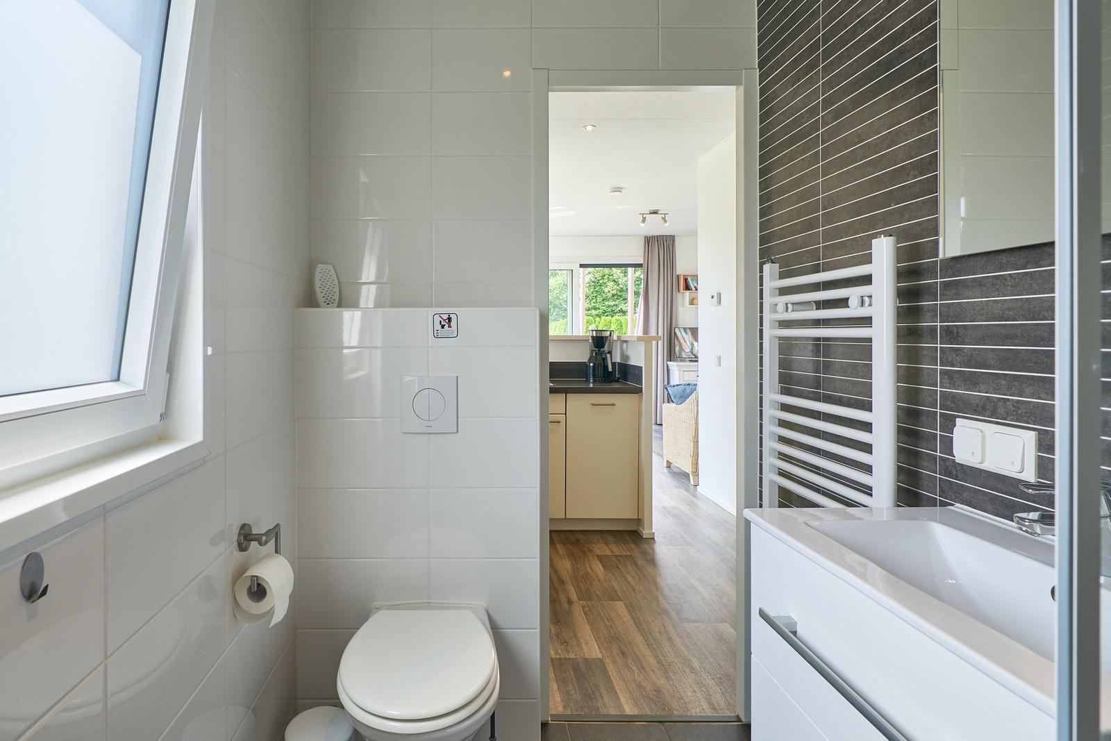 Badezimmer mit Toilette, Waschbecken und Heizkörper. Durchgang zu Küche und Wohnbereich.